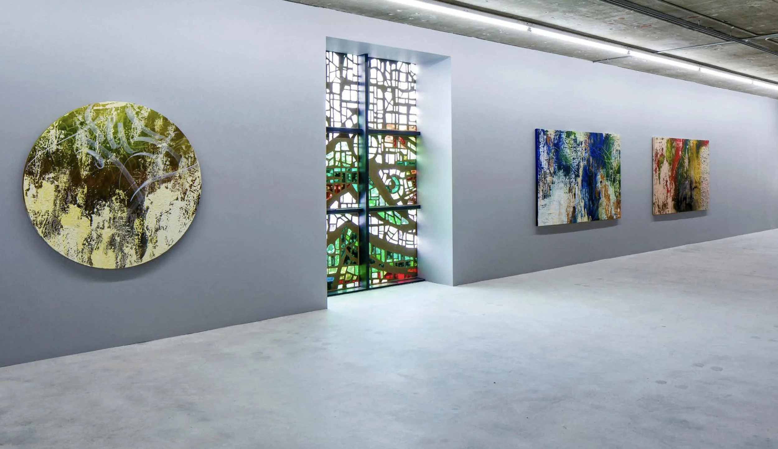 Gallery with three abstract paintings on a white wall and a colorful stained glass window in the center.