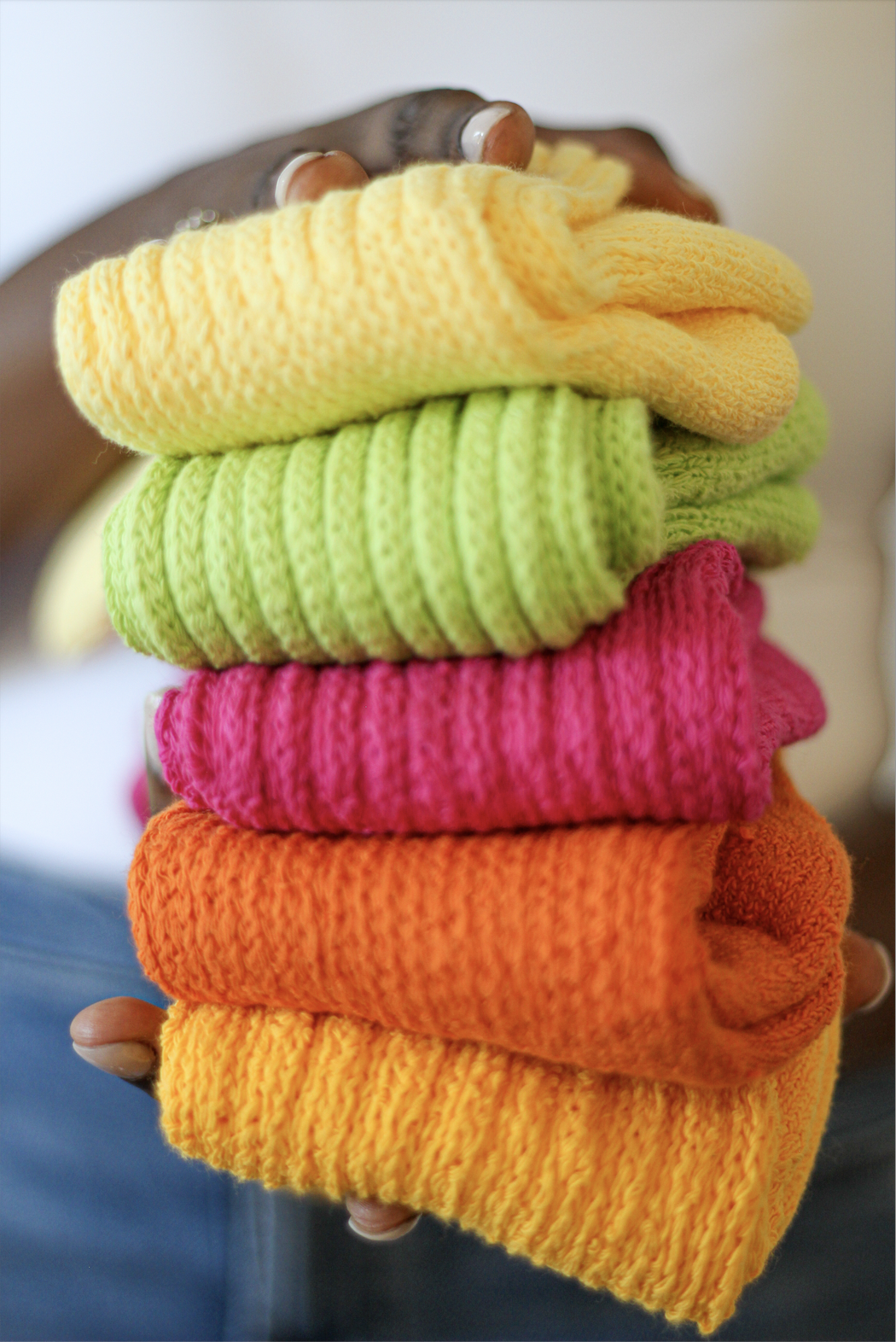 Person holding a stack of colorful knitted beanies in yellow, green, pink, orange, and yellow.