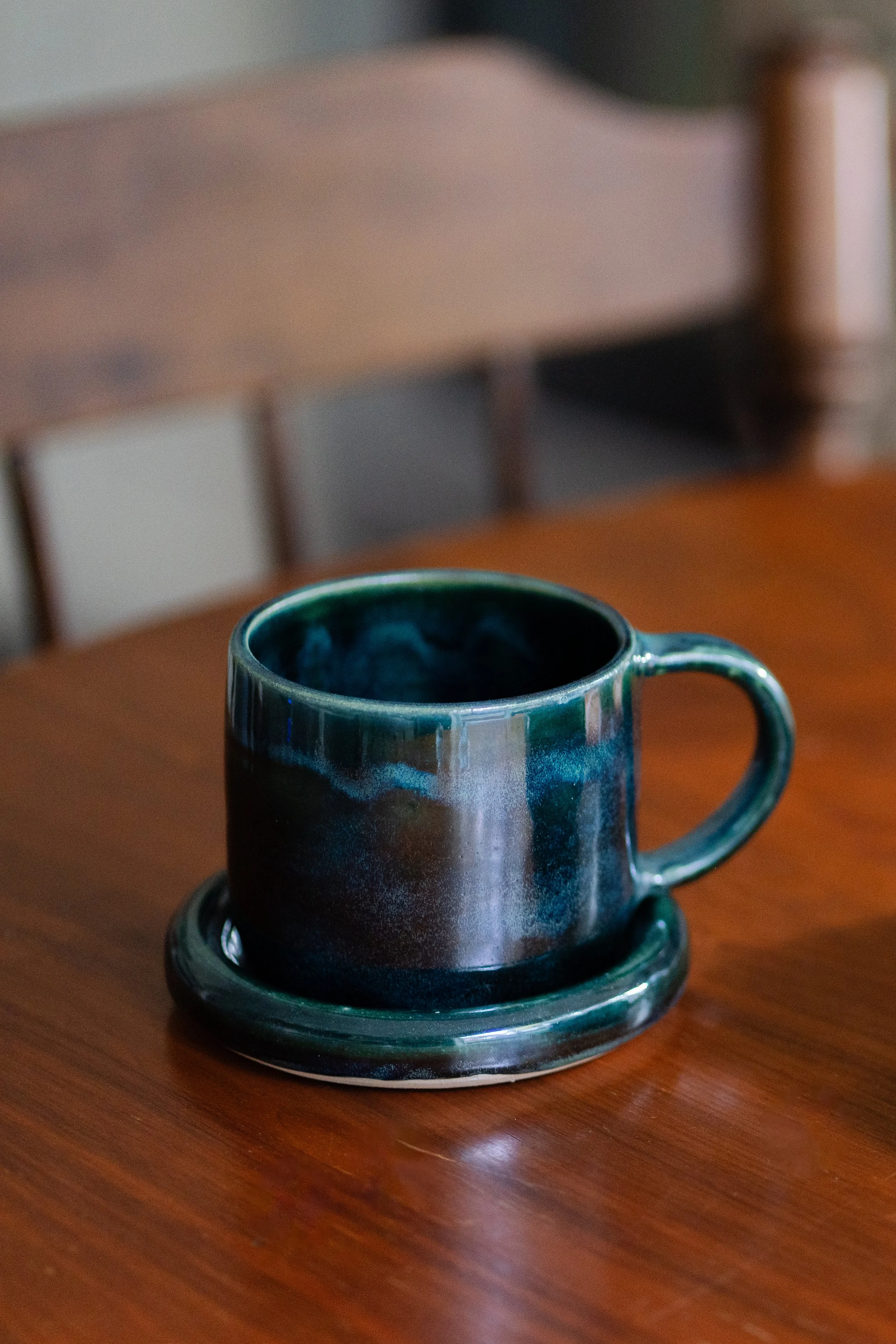 A navy blue ceramic mug sitting on a matching saucer on a wooden table.