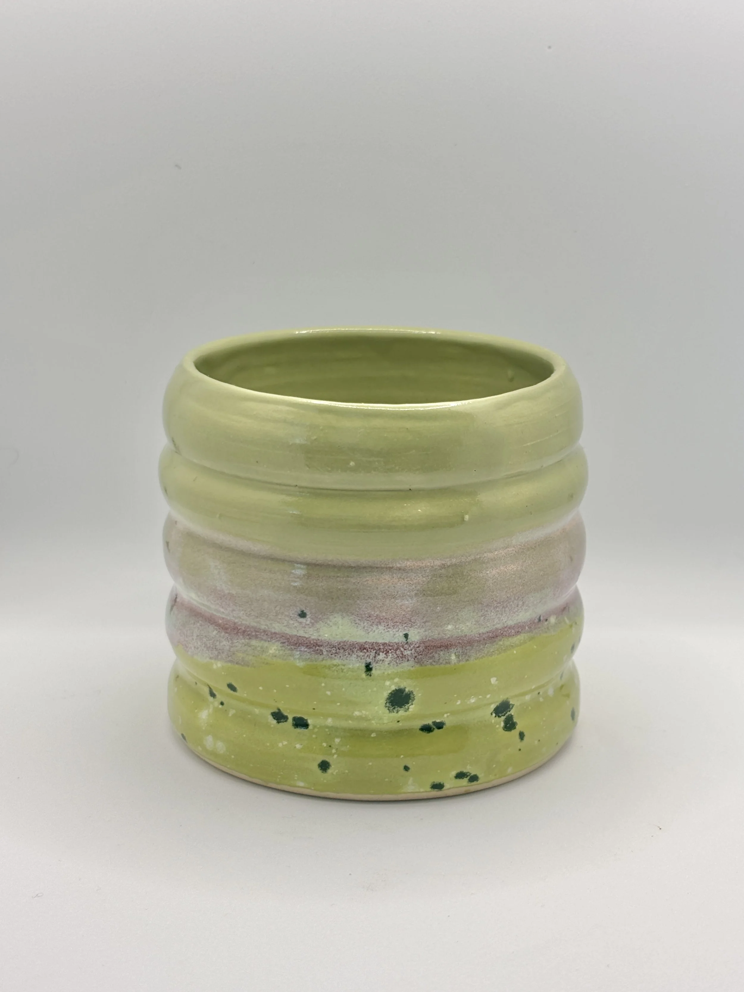 Green ceramic pot with ridges and splatter design on a plain white background.