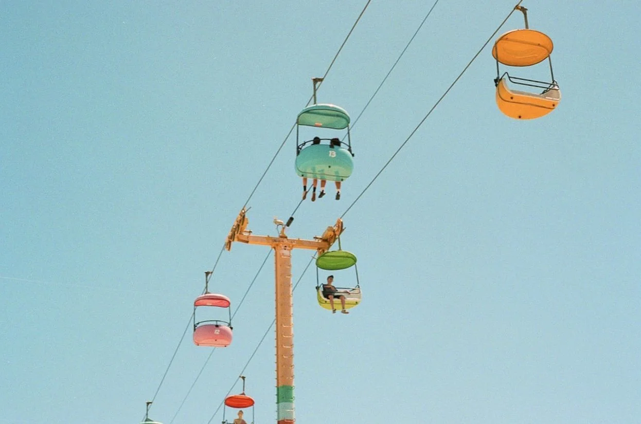 Colorful amusement park chairlift with several people riding against a clear blue sky.
