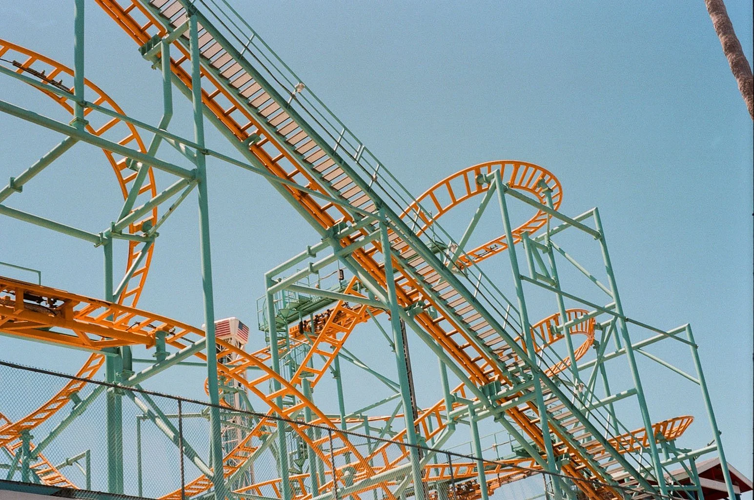 Colorful roller coaster with orange tracks and green supports against a clear blue sky.
