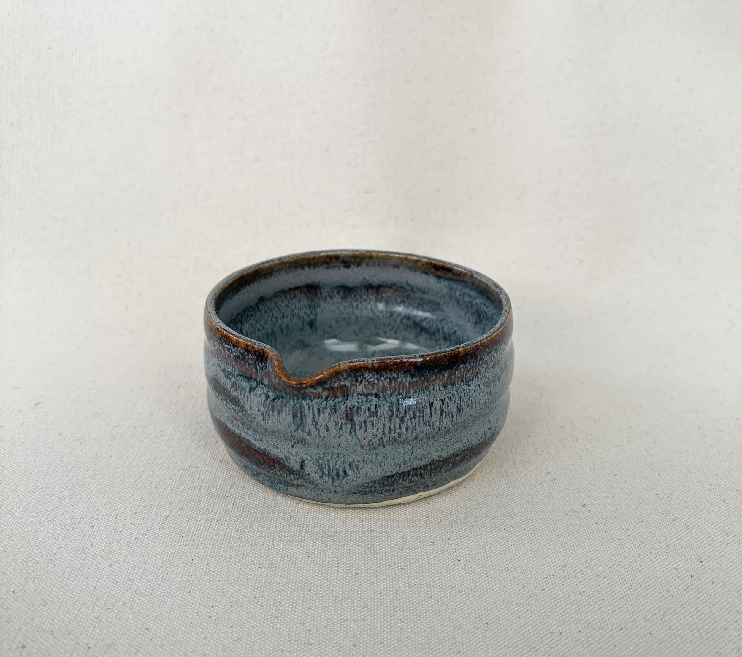 A small matcha bowl (chawan) with a blue and brown glaze, placed on a plain, light-colored surface.