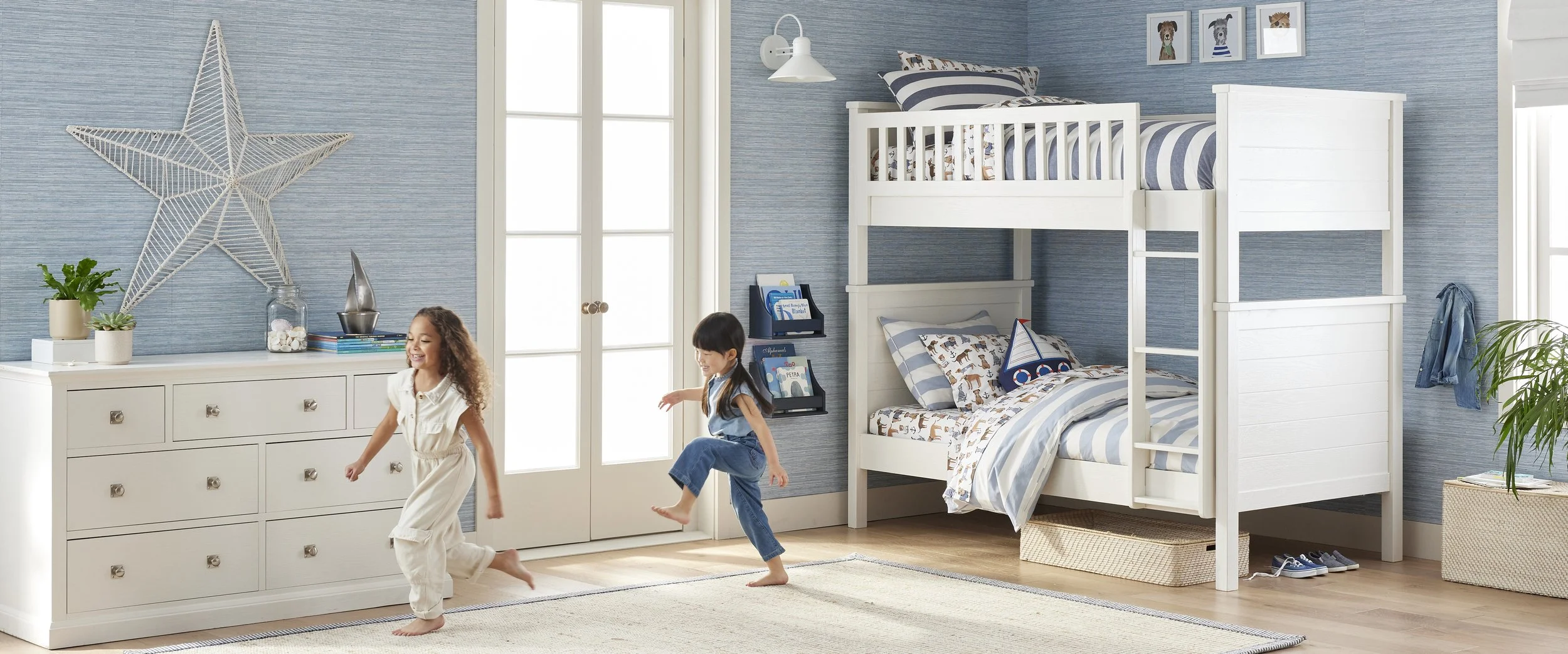 Two children playing in a bedroom with a bunk bed, blue walls, a white dresser, and wall art of animals.