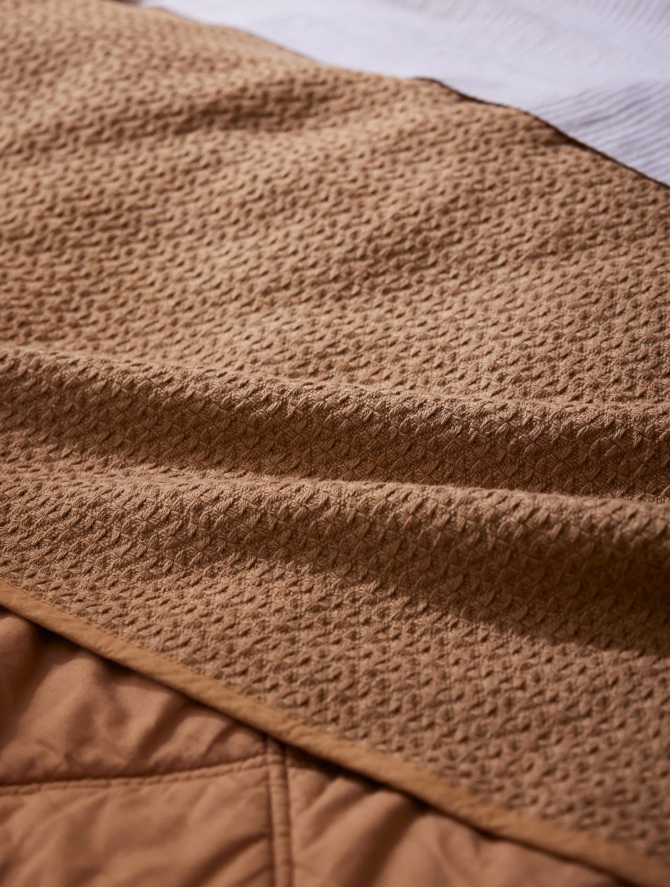 Close-up of brown textured fabric with a white top fabric in the background.