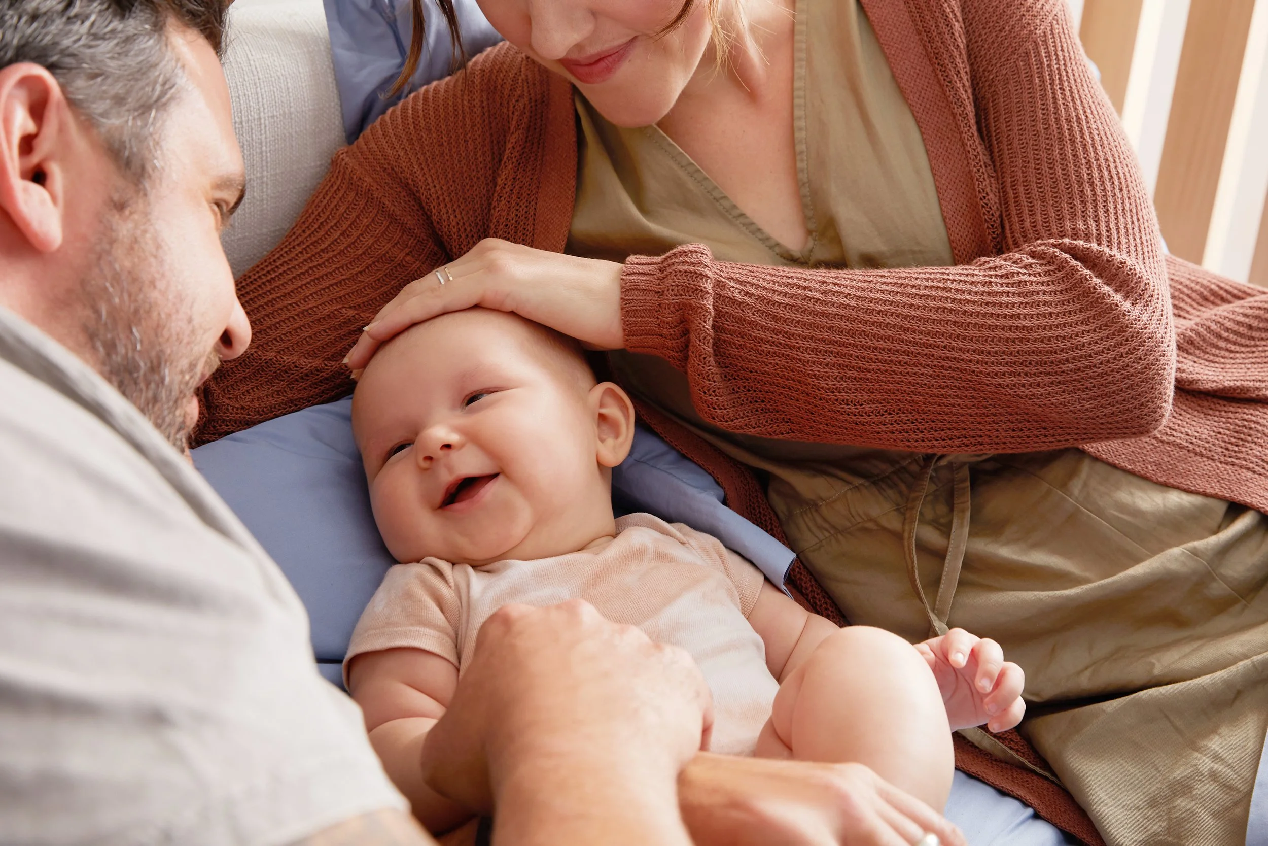 A close-up of a family with an elderly man, a woman, and a baby lying close together on a bed, smiling and enjoying a moment of affection.