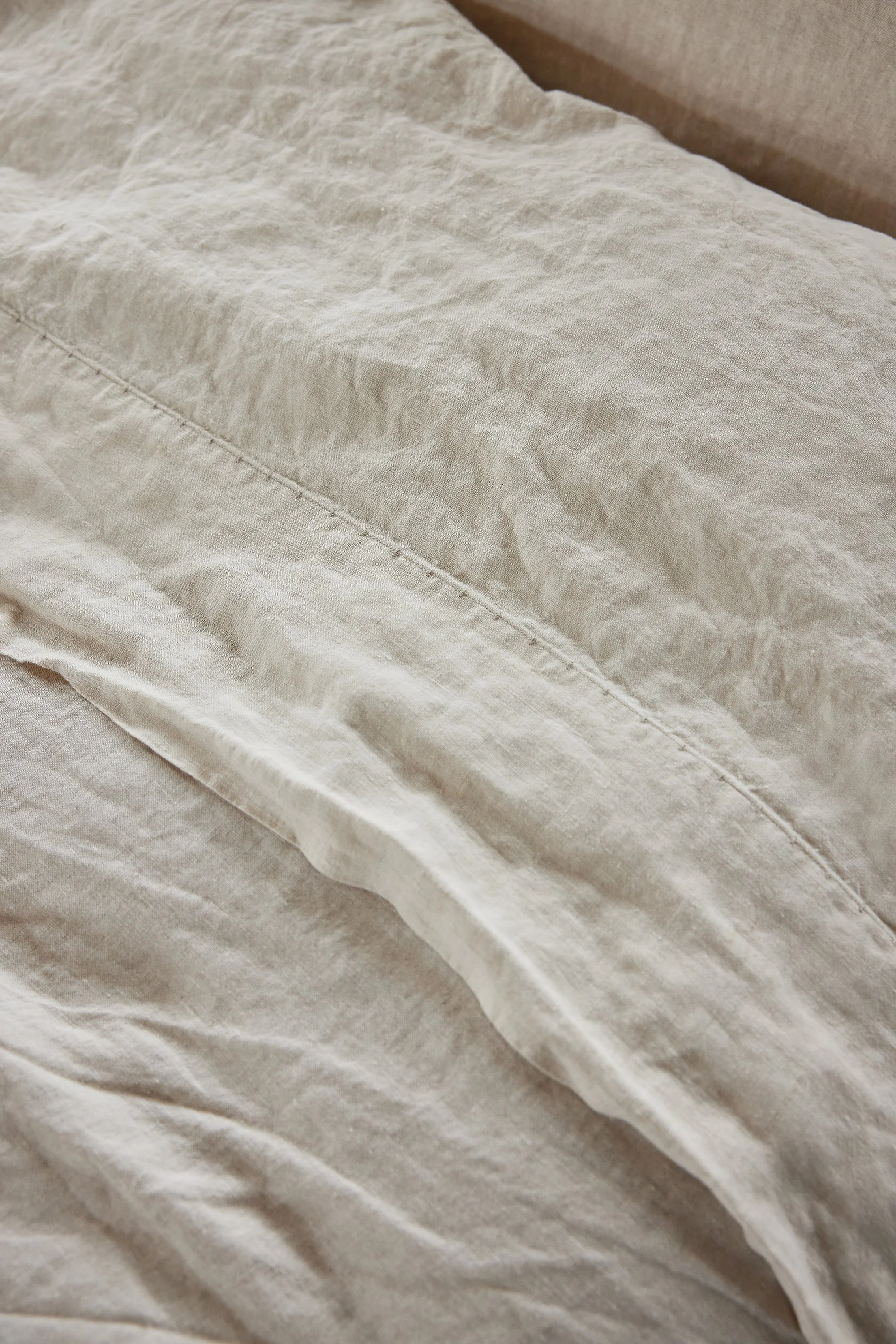 Close-up view of beige fabric with visible creases and stitching, possibly a bedsheet or curtain.