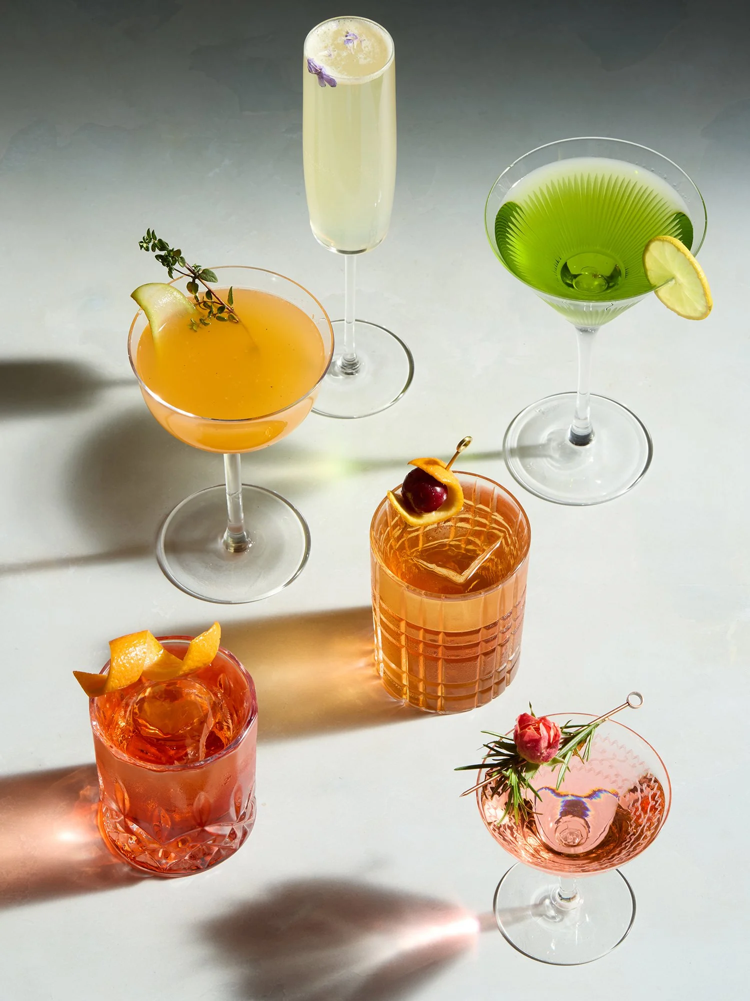 Various colorful cocktails with garnishes on a light surface.
