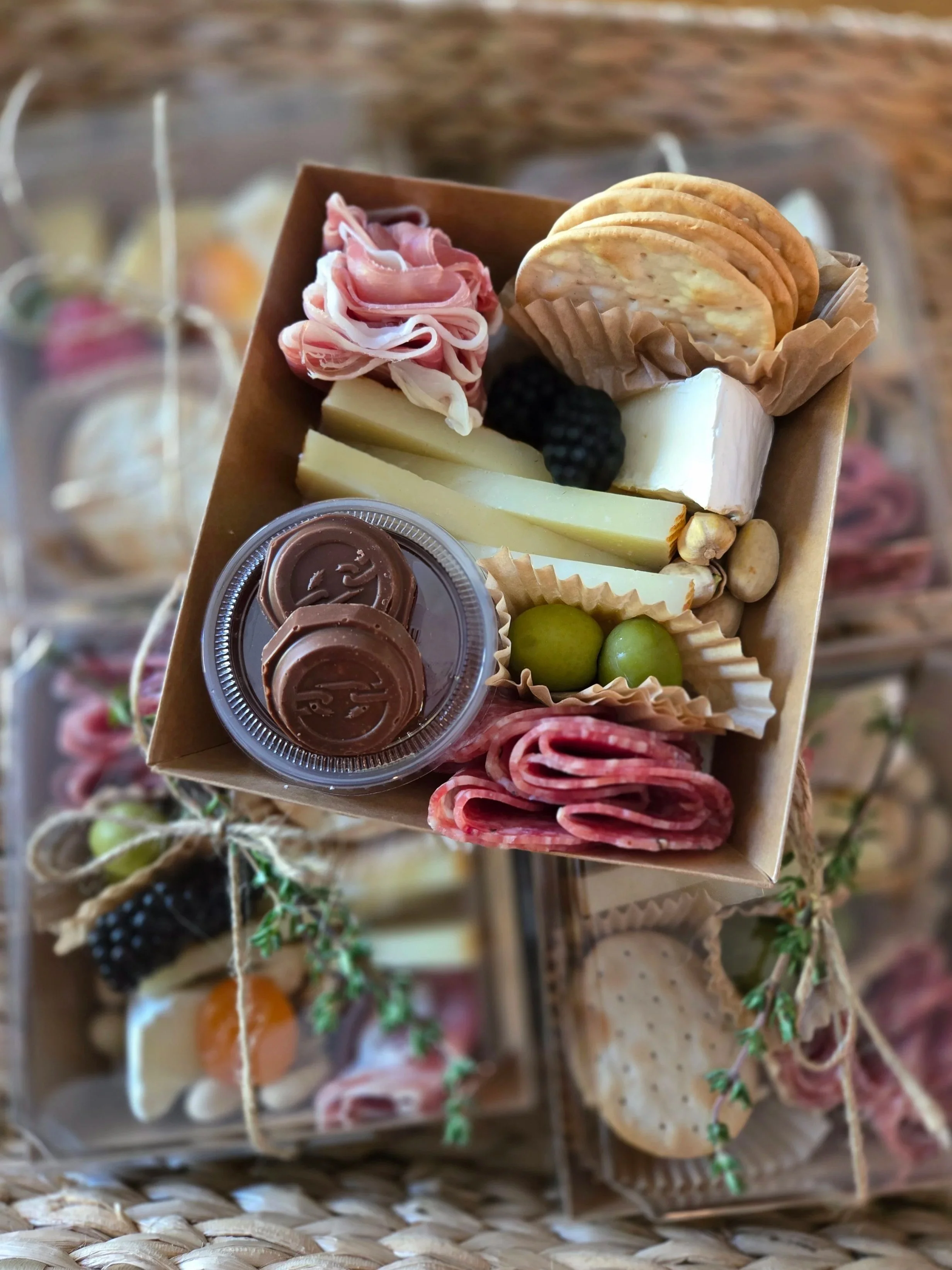 Miniature food assortment including cheese, crackers, cured meats, blackberries, green olives, and chocolates on a wooden display