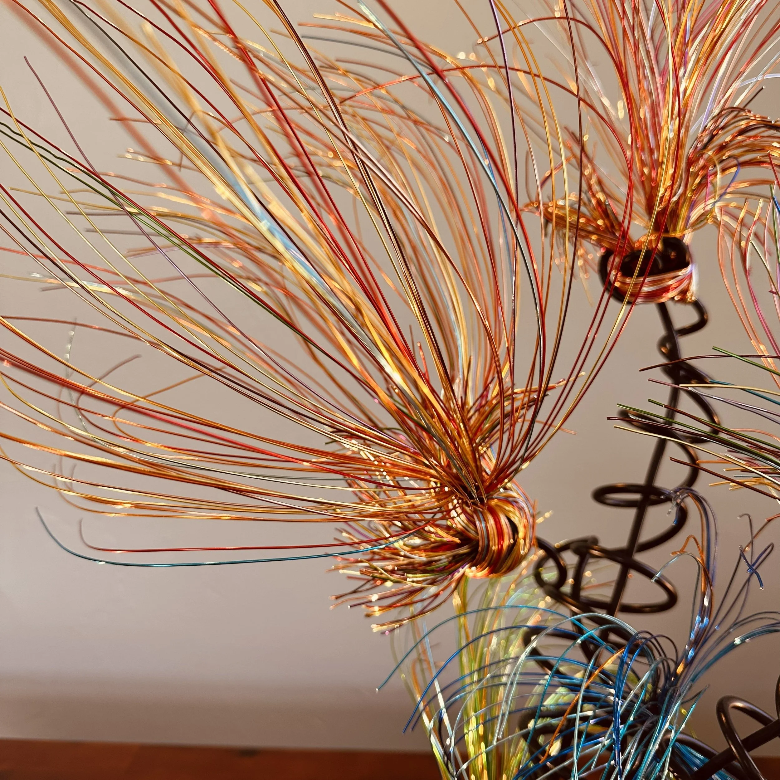Title:  "Luminous" 
Dimensions:  2' × 2 '× 2' 8”
Description: Fine wires flare outward like petals deciding to open, catching the light in shifting tones of copper, ember, and moss. The piece holds the stillness of a plant just on the edge of becomin