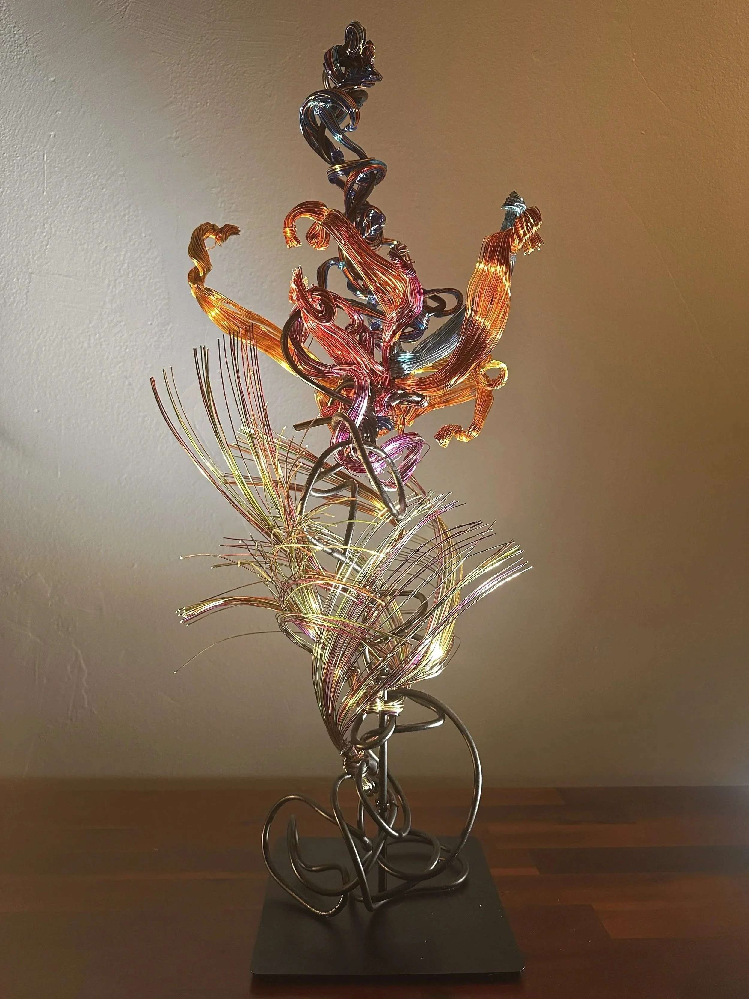 Title: “Paradise"   Spot Lighting. 
Dimensions:  1' 0" × 1' 0" × 2' 8"
Coiled strands rise and twist like a wild tendril caught in a sudden gust, capturing the restless motion of growth reaching toward open air.



Hand‑formed wire sculpture explorin