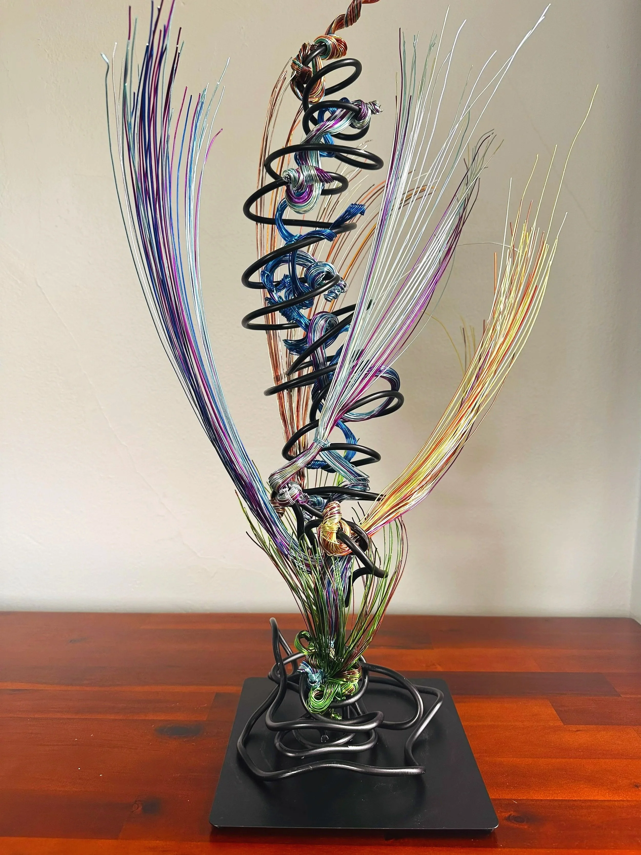 Title: "Rising"" View from front.
Dimensions:   1' 6" × 1' 6" × 2' 5"
The form stretches upward, its strands leaning into imagined air. A sculpture that feels mid‑movement — rooted below, reaching toward whatever shift is happening above. 