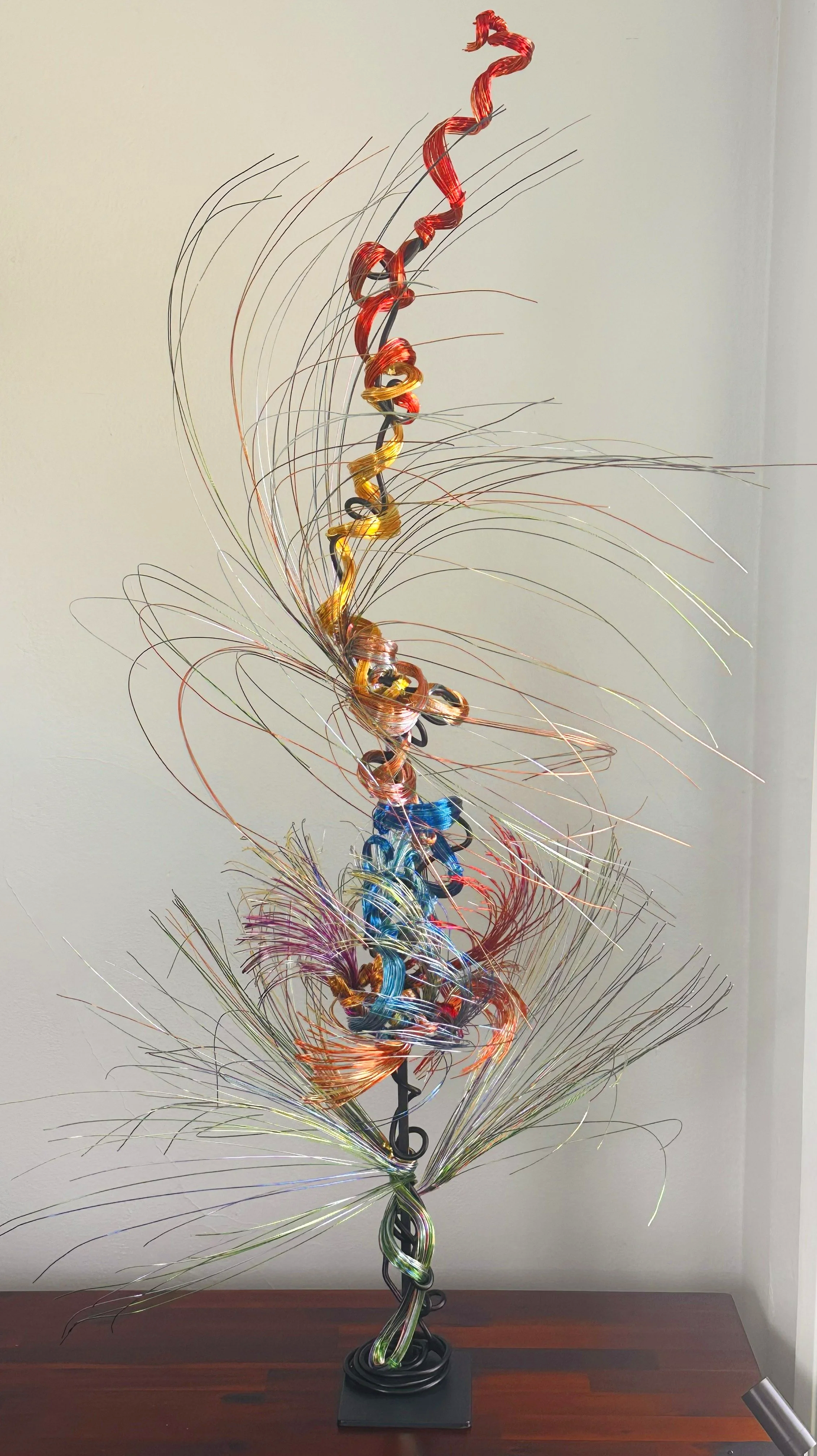 Title: Aglow in Motion 
Dimension. 2" x 2" x 4".8' 
This piece explores the soft resilience of floral forms — branches lifting, colors gathering, and thin lines swaying as if touched by light. Shaped slowly by hand, this commissioned piece carries bo