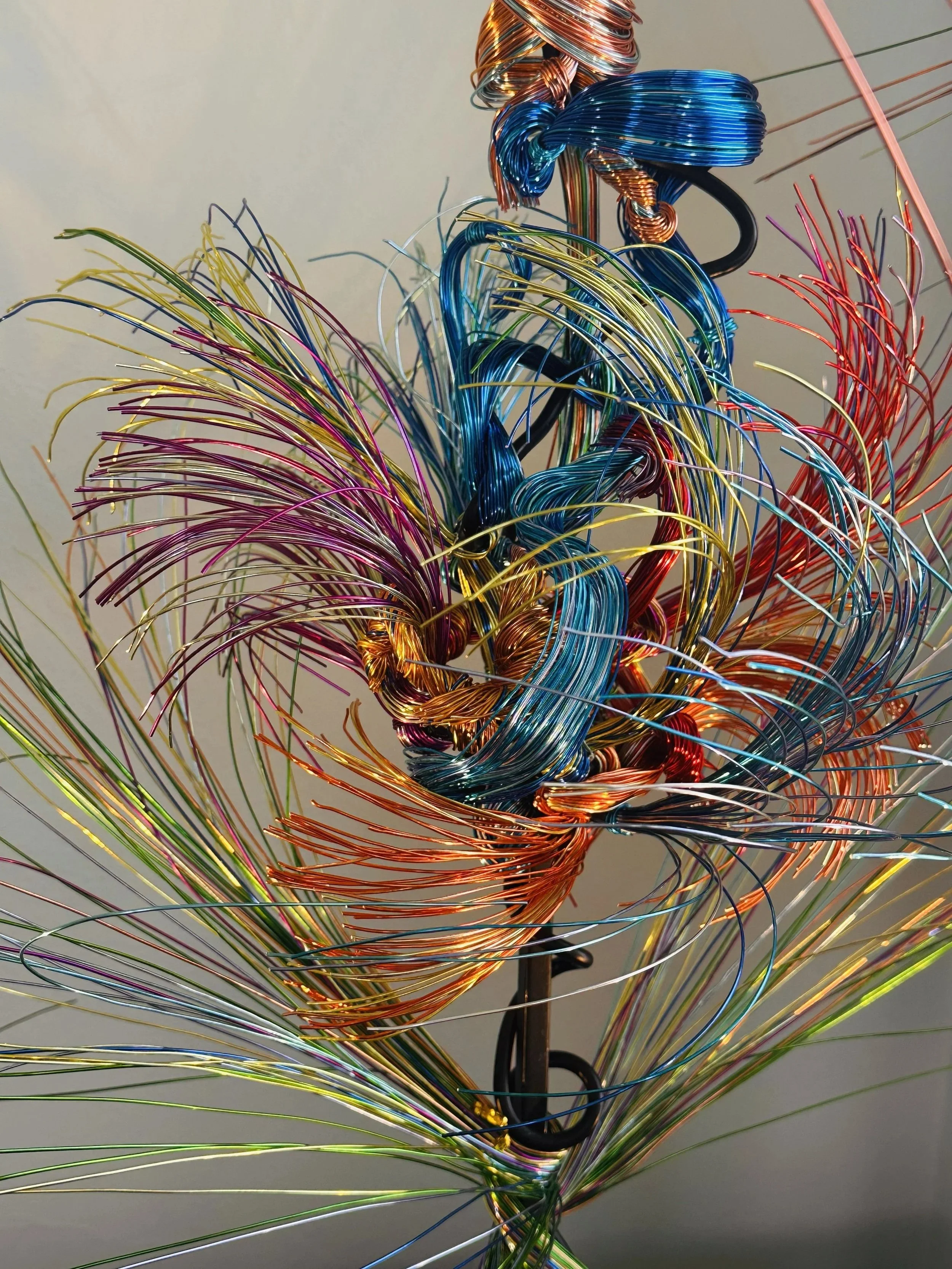 Title: Aglow in Motion. Center detail view #3 
Dimension. 2" x 2" x 4".8' 
This piece explores the soft resilience of floral forms — branches lifting, colors gathering, and thin lines swaying as if touched by light. Shaped slowly by hand, this commis