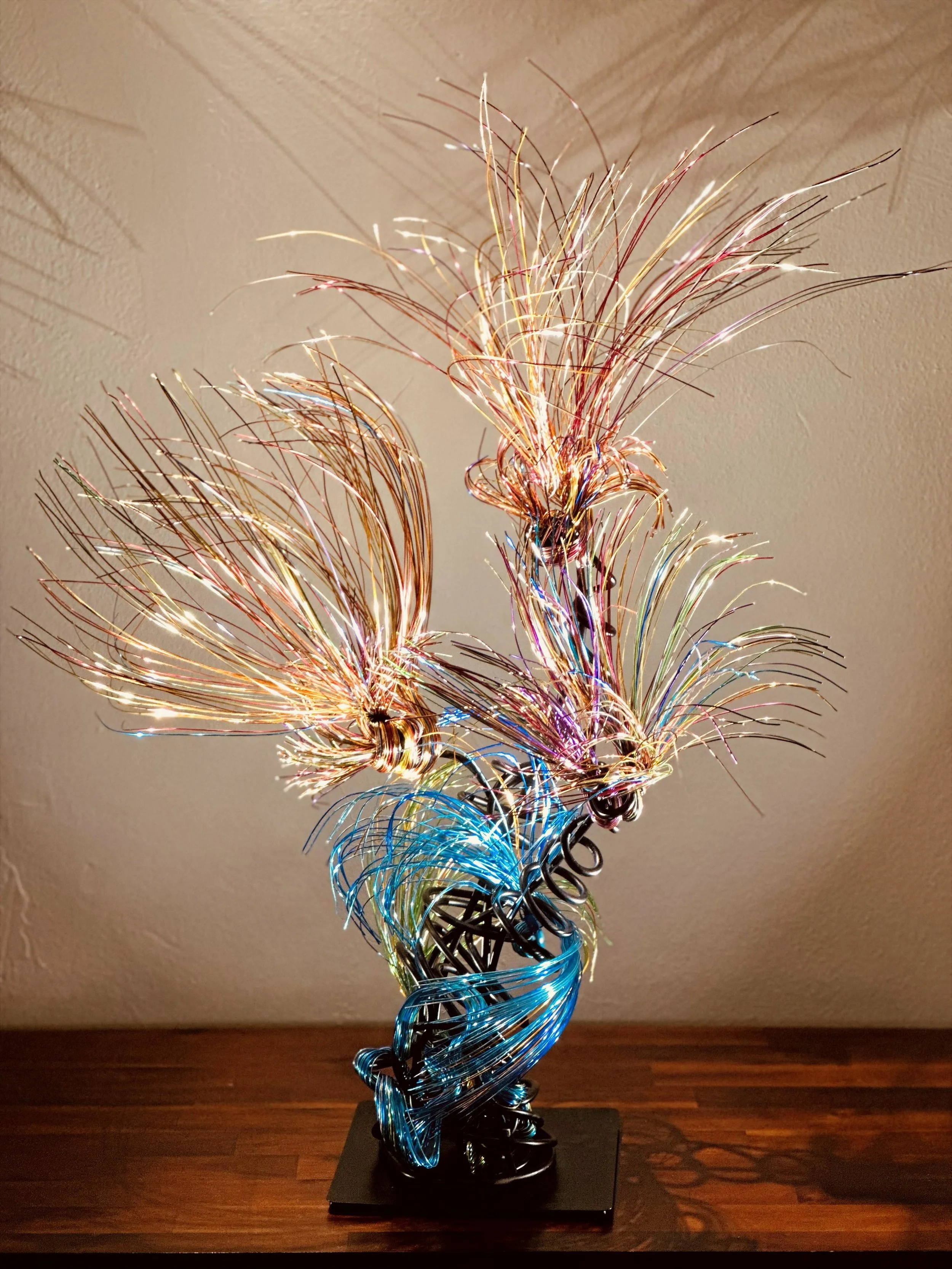 Title:  "Luminous"
Dimensions: 2' × 2 '× 2' 8” 
Description: Fine wires flare outward like petals deciding to open, catching the light in shifting tones of copper, ember, and moss. The piece holds the stillness of a plant just on the edge of becoming