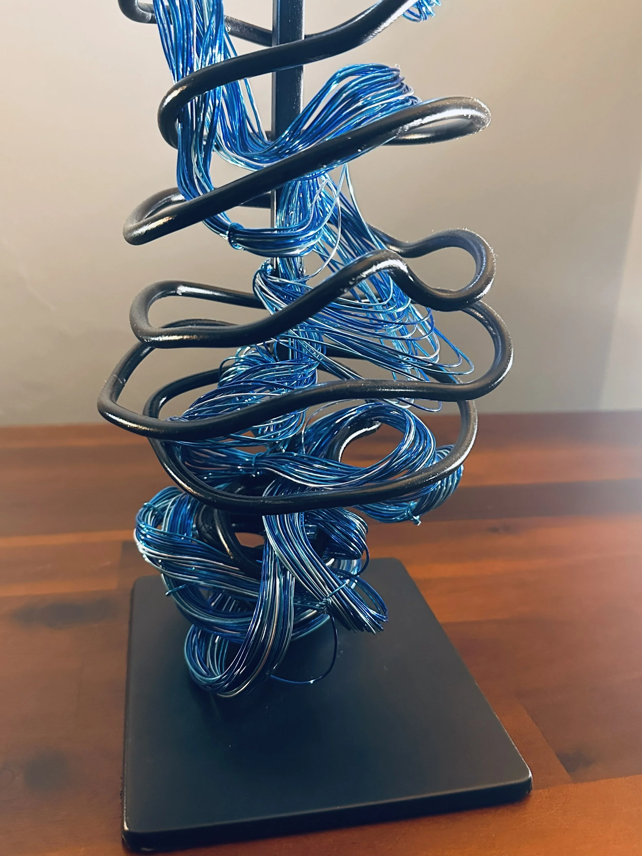 Title:  "Gentle Breeze" View of base. 
Dimensions: 3' 6" x 3' 6" x 4 '10" 
From a dense, coiled base, the wires rise like the trunk of a young palm, opening into a crown of wind‑caught fronds. 