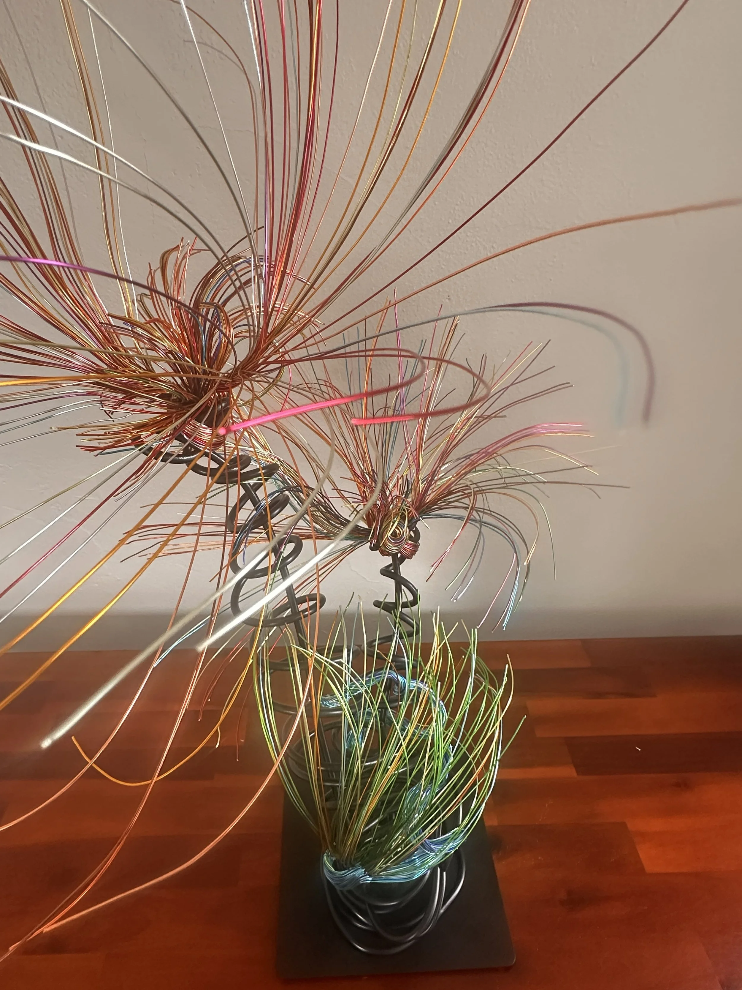 Title: Luminous. Aerial View
Dimensions:  2' × 2 '× 2' 8"
Fine wires flare outward like petals deciding to open, catching the light in shifting tones of copper, ember, and moss. The piece holds the stillness of a plant just on the edge of becoming so