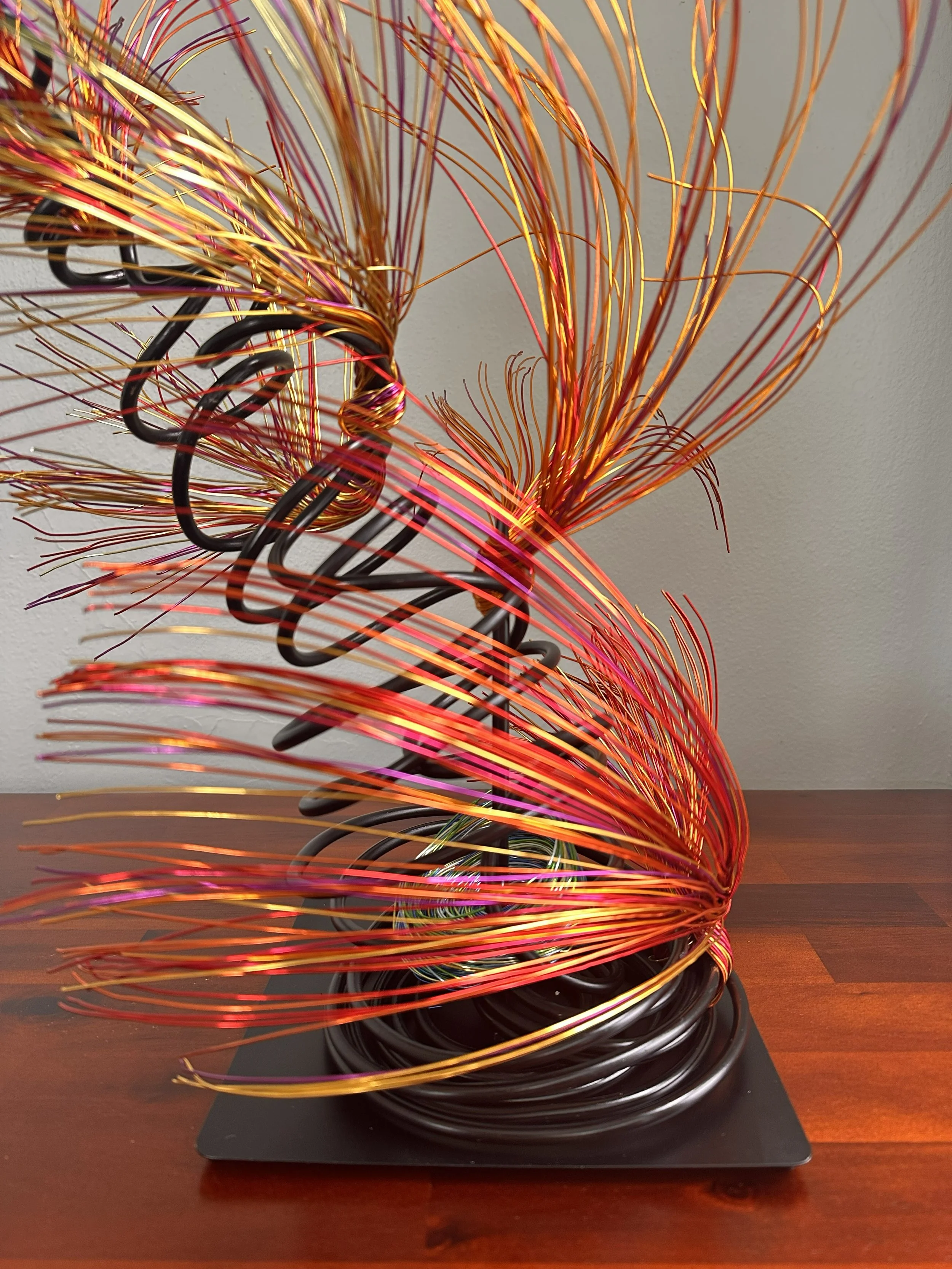 Title: "Flowing" View from front 
Dimensions: 1' × 1' × 2'
 Red and Orange wire rises from a grounded base into a quiet, upward motion — a gesture shaped slowly by hand, carrying both volcanic tension and blue wave lift