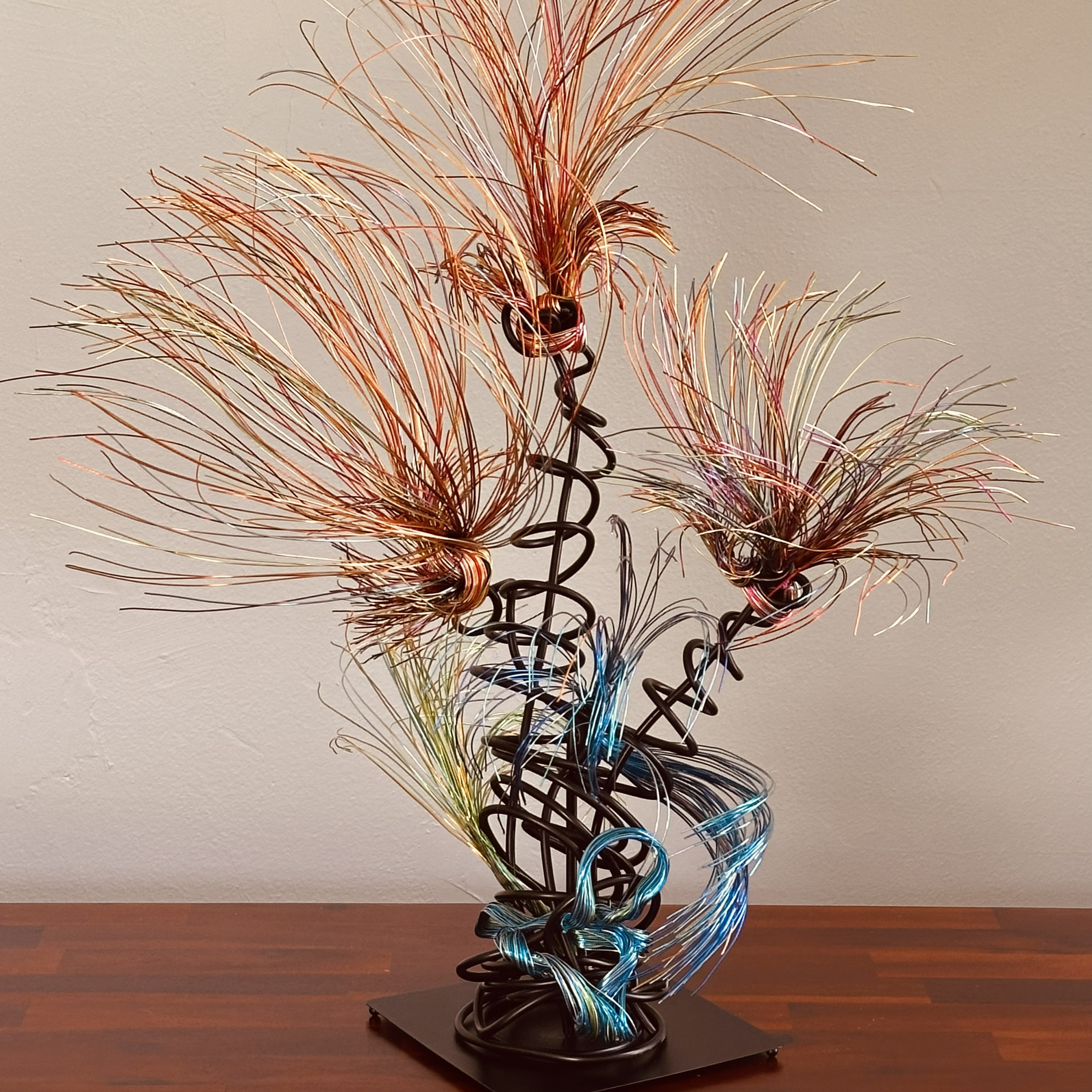 Title:  "Luminous" 
Dimensions:  2' × 2 '× 2' 8”
Description: Fine wires flare outward like petals deciding to open, catching the light in shifting tones of copper, ember, and moss. The piece holds the stillness of a plant just on the edge of becomin