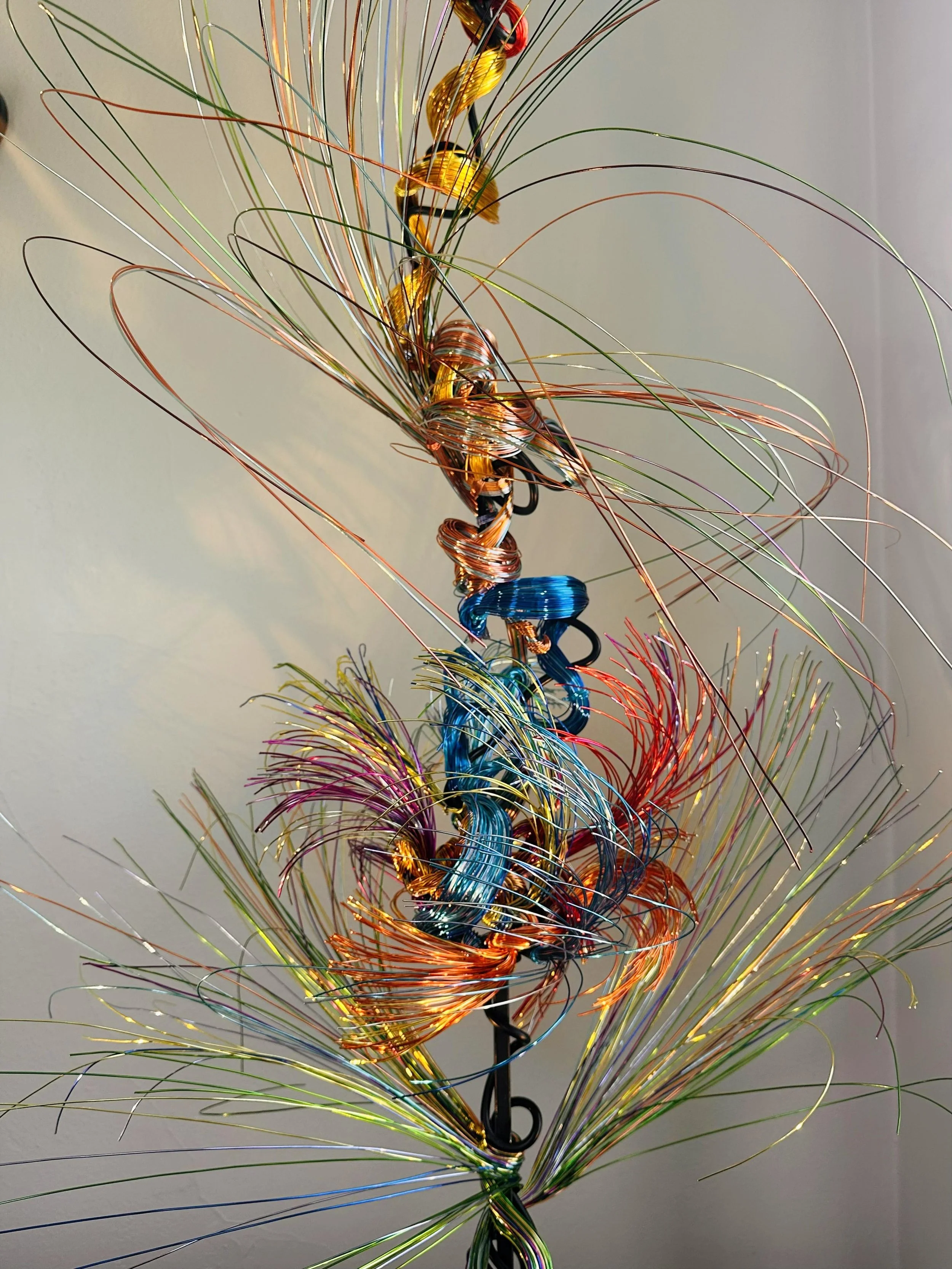 Title: Aglow in Motion with spot lighting Dimension. 2" x 2" x 4".8' 
This piece explores the soft resilience of floral forms — branches lifting, colors gathering, and thin lines swaying as if touched by light. Shaped slowly by hand, this commissione