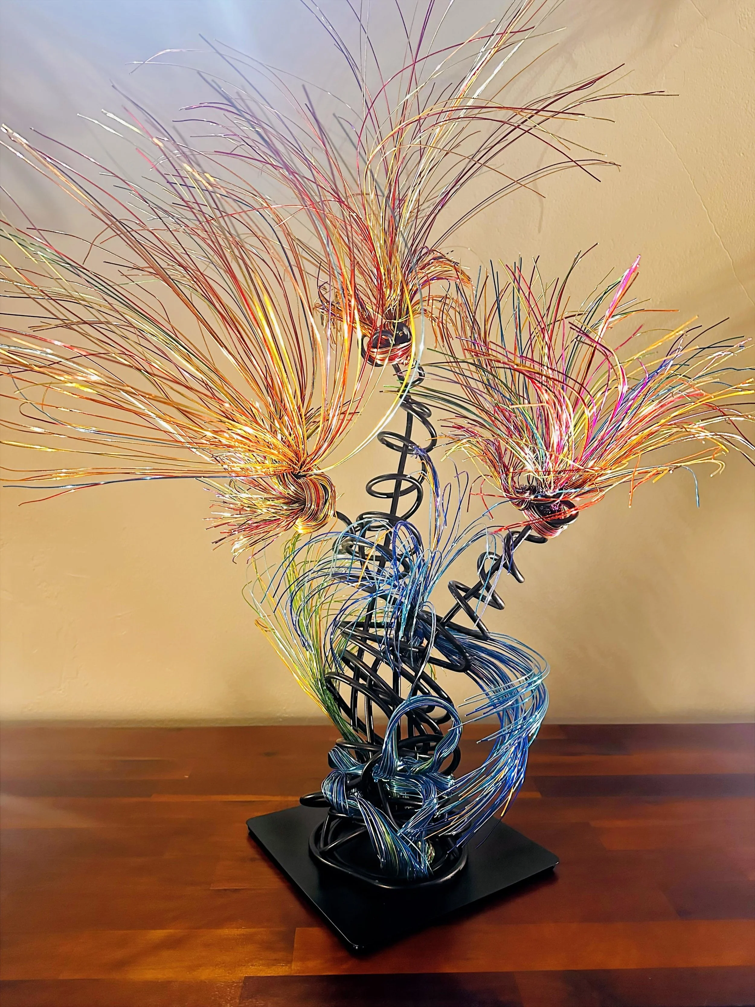 Title:  "Luminous" 
Dimensions:  2' × 2 '× 2' 8”
Description: Fine wires flare outward like petals deciding to open, catching the light in shifting tones of copper, ember, and moss. The piece holds the stillness of a plant just on the edge of becomin