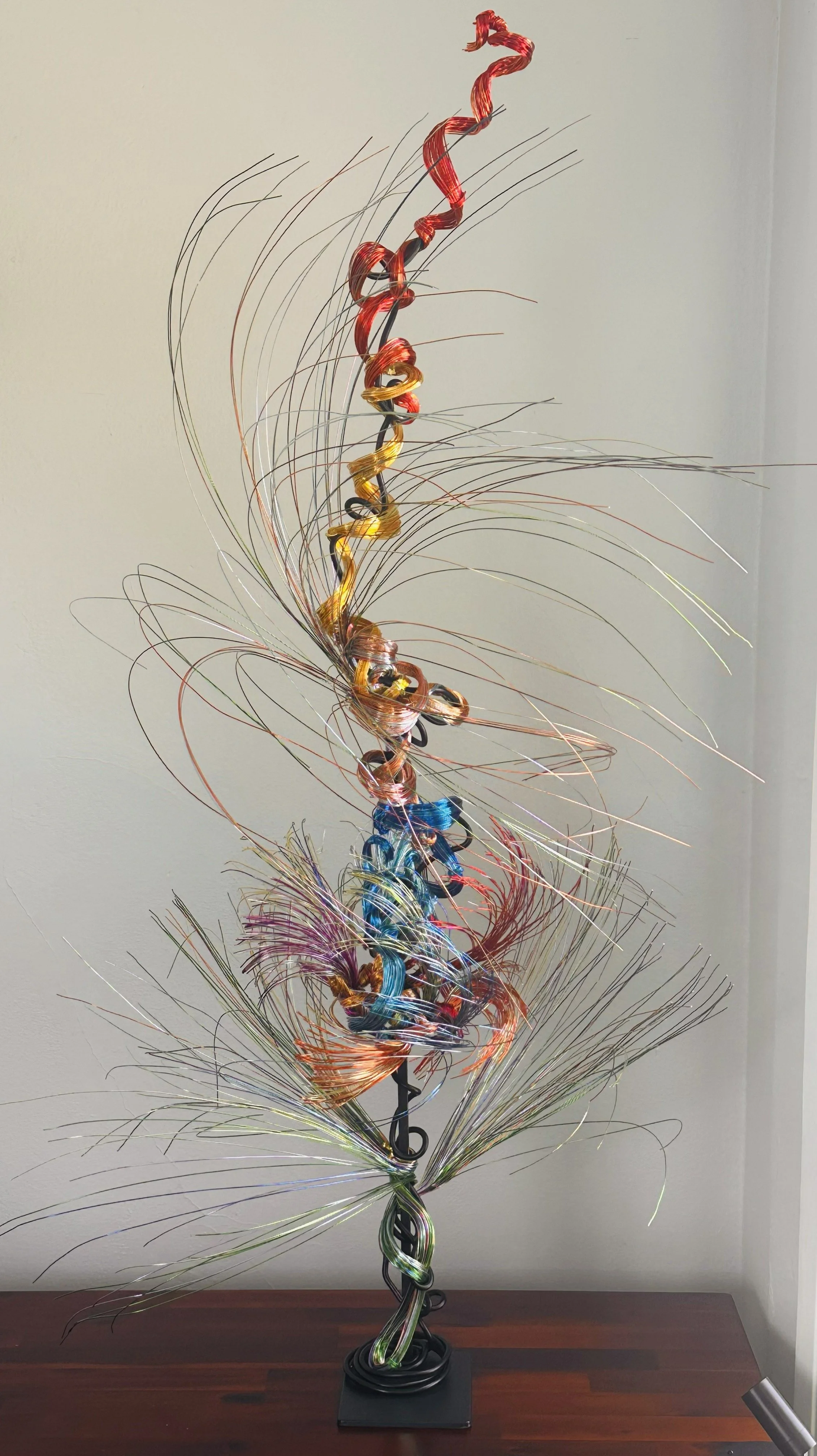  Title: Aglow in Motion with spot lighting Dimension. 2" x 2" x 4".8' 
This piece explores the soft resilience of floral forms — branches lifting, colors gathering, and thin lines swaying as if touched by light. Shaped slowly by hand, this commission