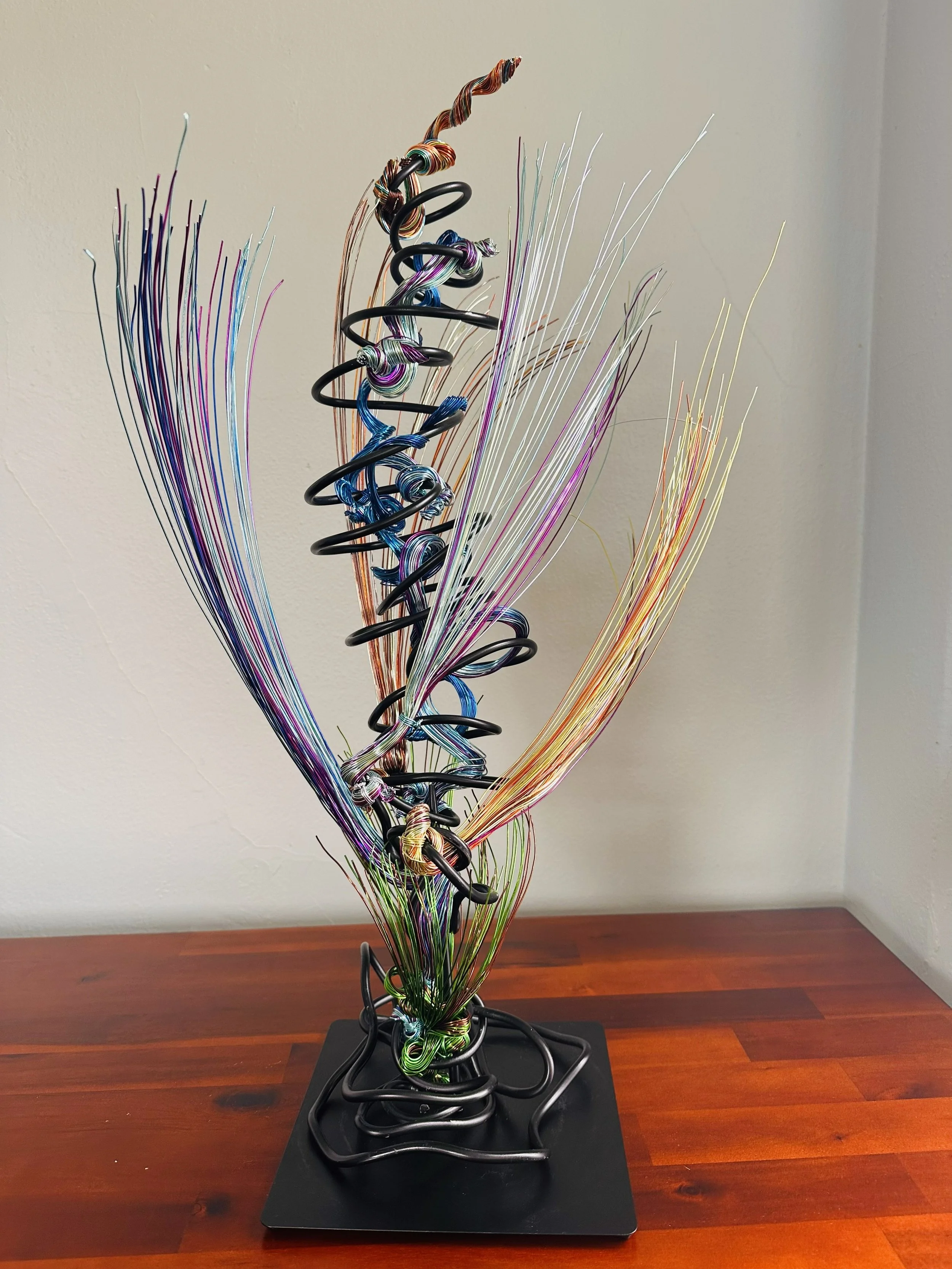 Title: "Rising"" View from front.
Dimensions:   1' 6" × 1' 6" × 2' 5"
The form stretches upward, its strands leaning into imagined air. A sculpture that feels mid‑movement — rooted below, reaching toward whatever shift is happening above. 