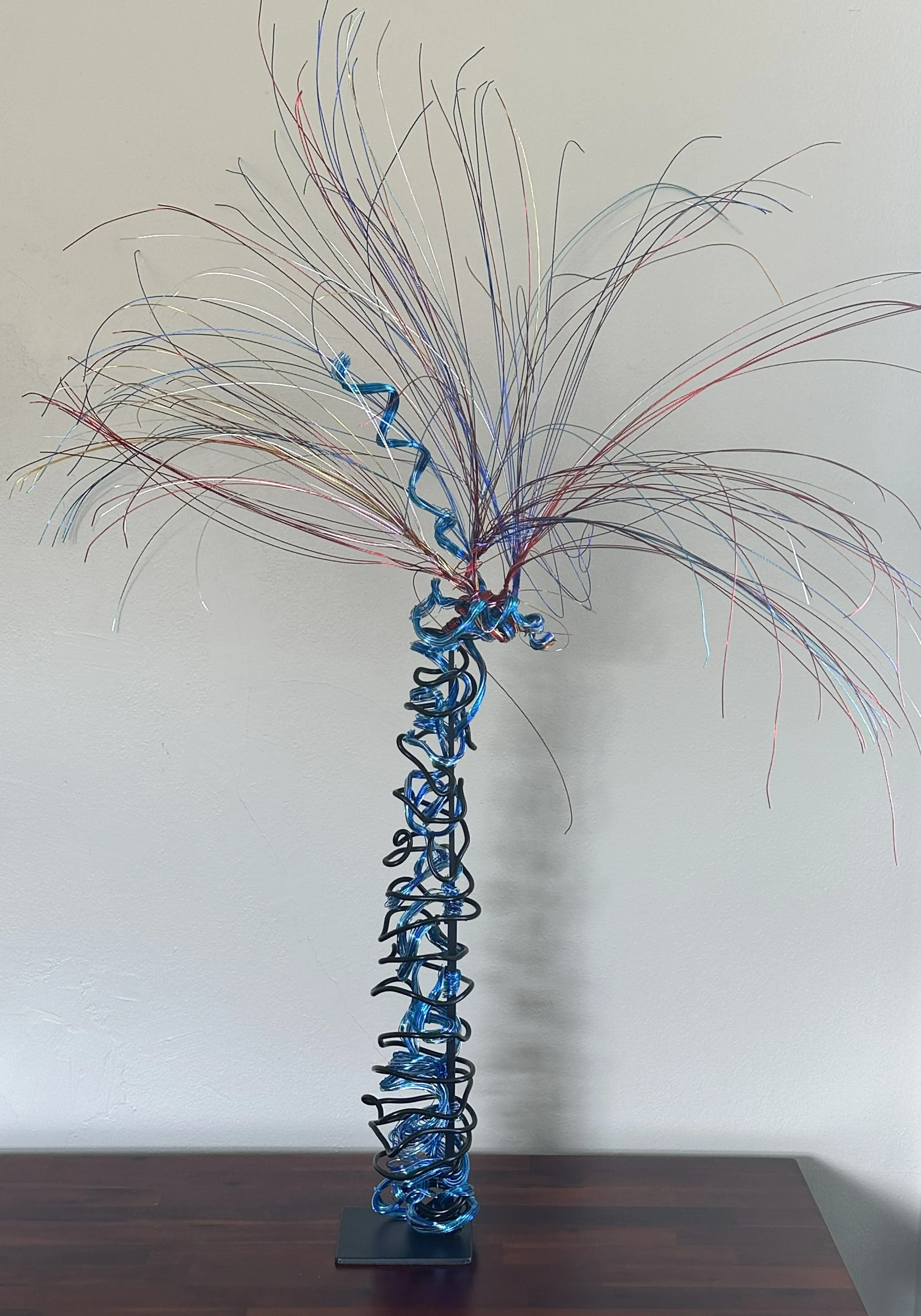 Title:  "Gentle Breeze" View from front.
Dimensions: 3' 6" x 3' 6" x 4 '10" 
From a dense, coiled base, the wires rise like the trunk of a young palm, opening into a crown of wind‑caught fronds. 



Hand‑formed wire sculpture exploring botanical moti