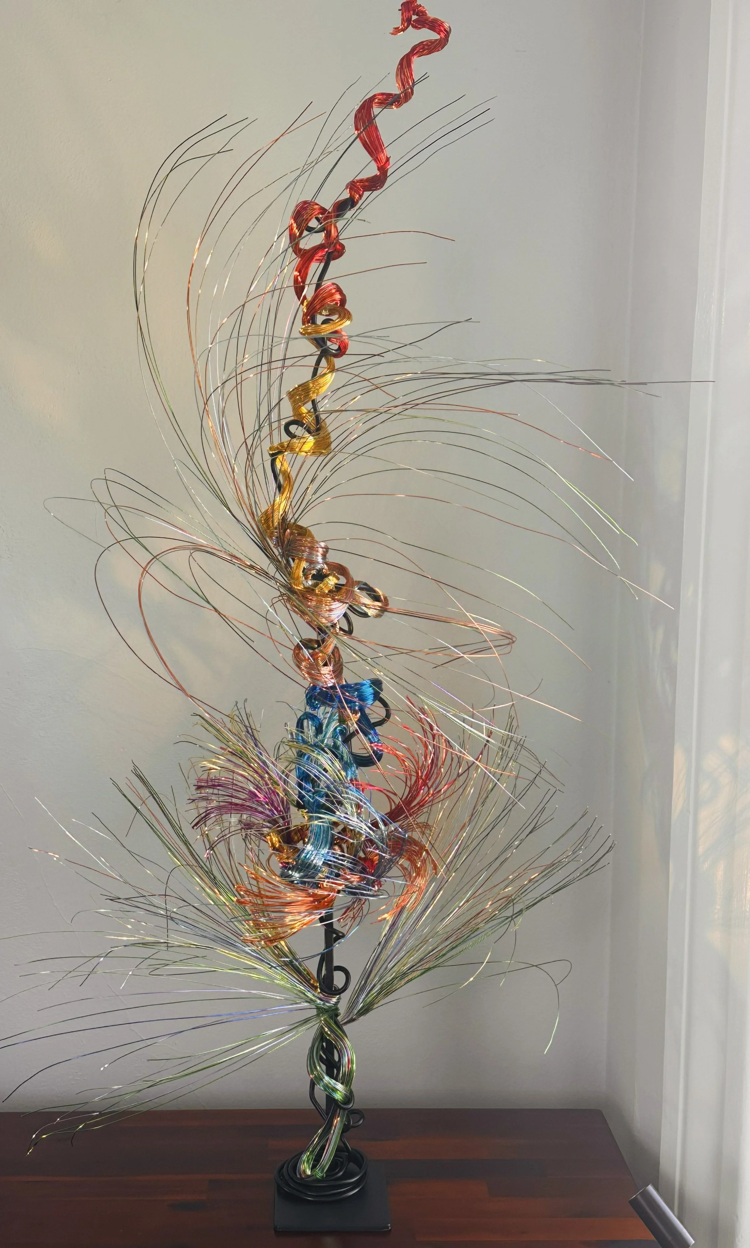 Title: Aglow in Motion 
Dimension. 2" x 2" x 4".8' 
This piece explores the soft resilience of floral forms — branches lifting, colors gathering, and thin lines swaying as if touched by light. Shaped slowly by hand, this commissioned piece carries bo