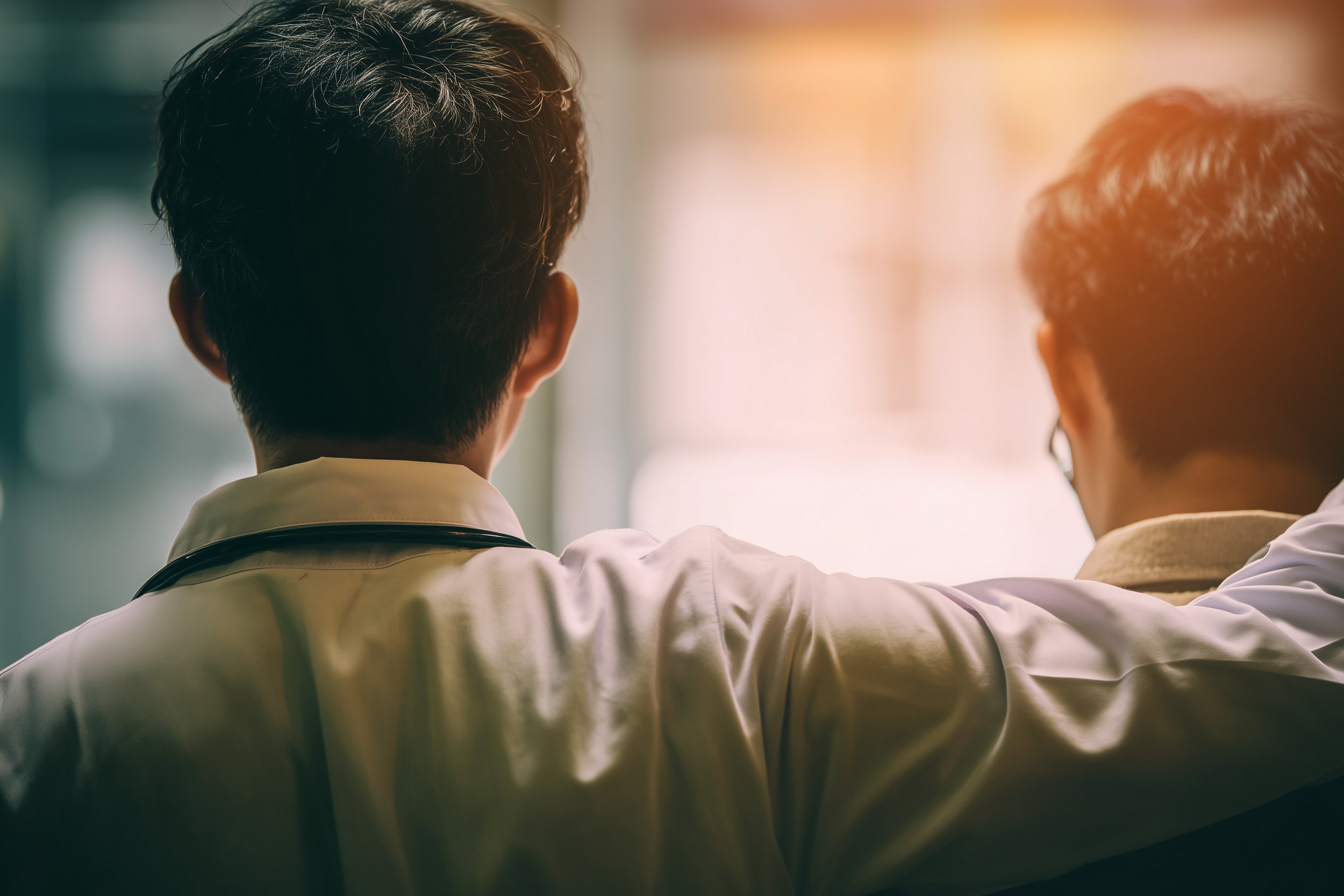 Two male doctors with a stethoscope looking out a window.