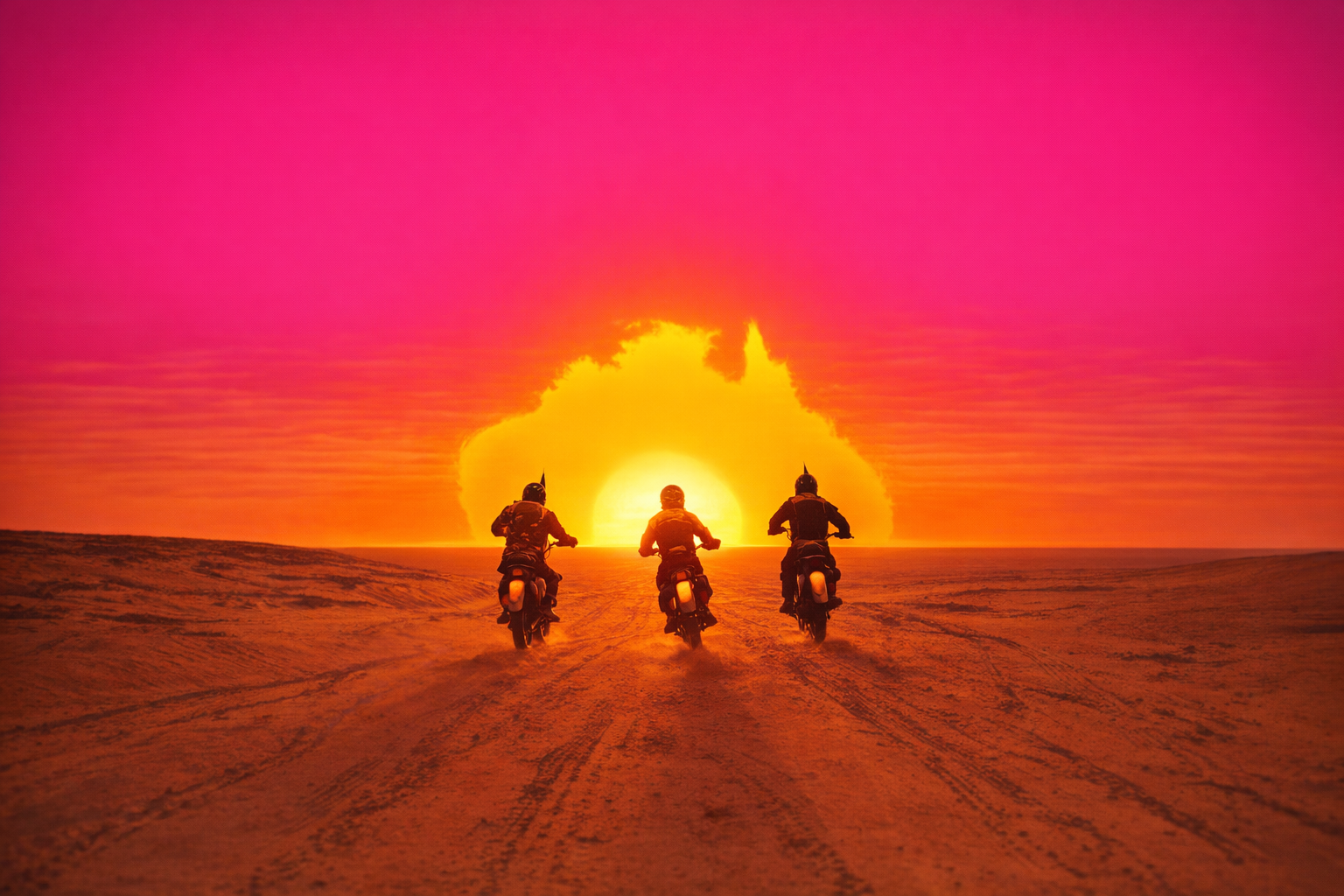 Three people riding motorcycles across a desert at sunset with a colorful pink, orange, and yellow sky and large clouds in the background.