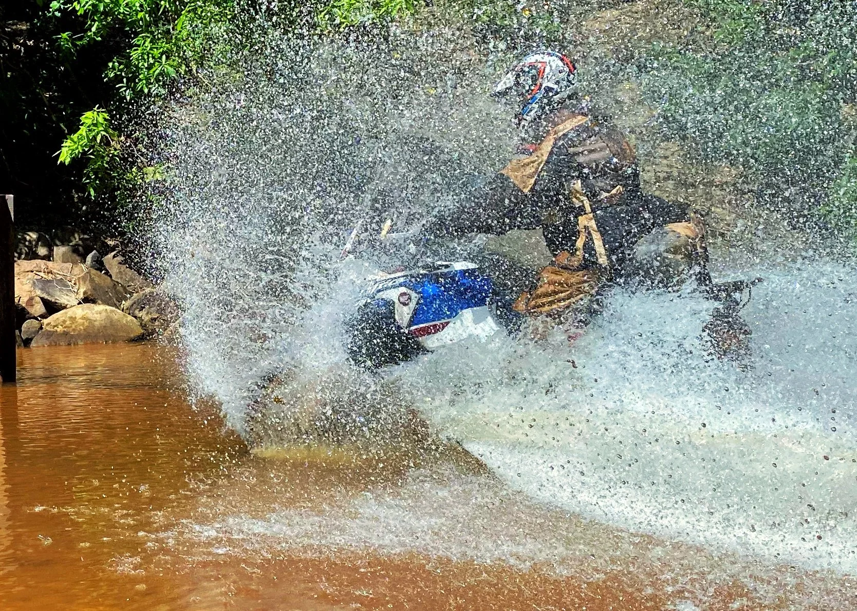 Motorcycle rider wearing a helmet and protective gear crashing into water and splashing.