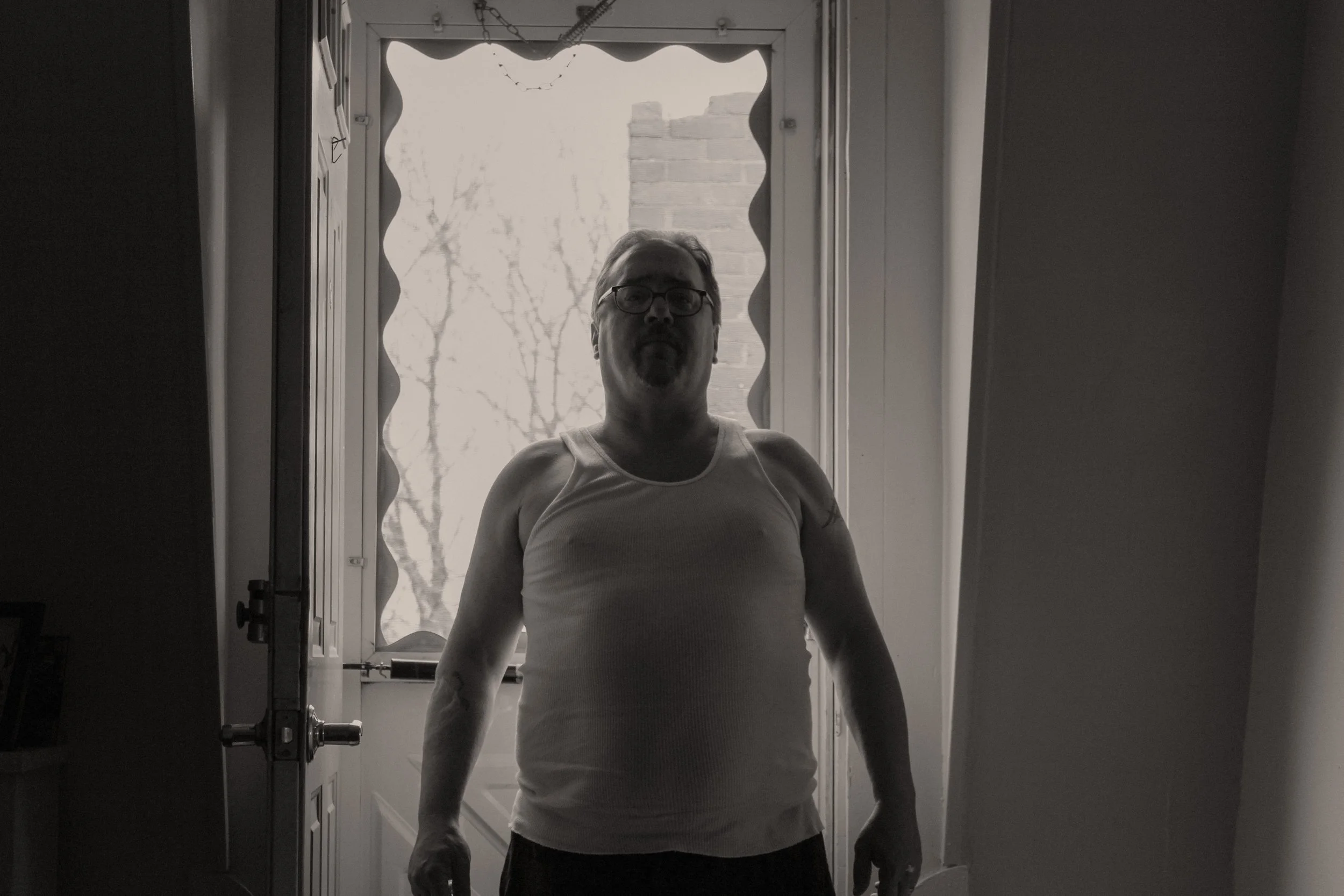 Man stands in front of door, back lit by the outside