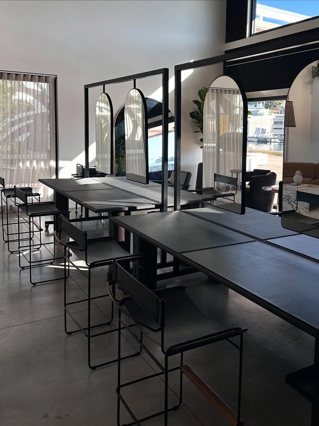 Modern interior of a restaurant or cafe with black tables and chairs, dividers with oval mirrors, natural lighting, large window, and minimal decor.