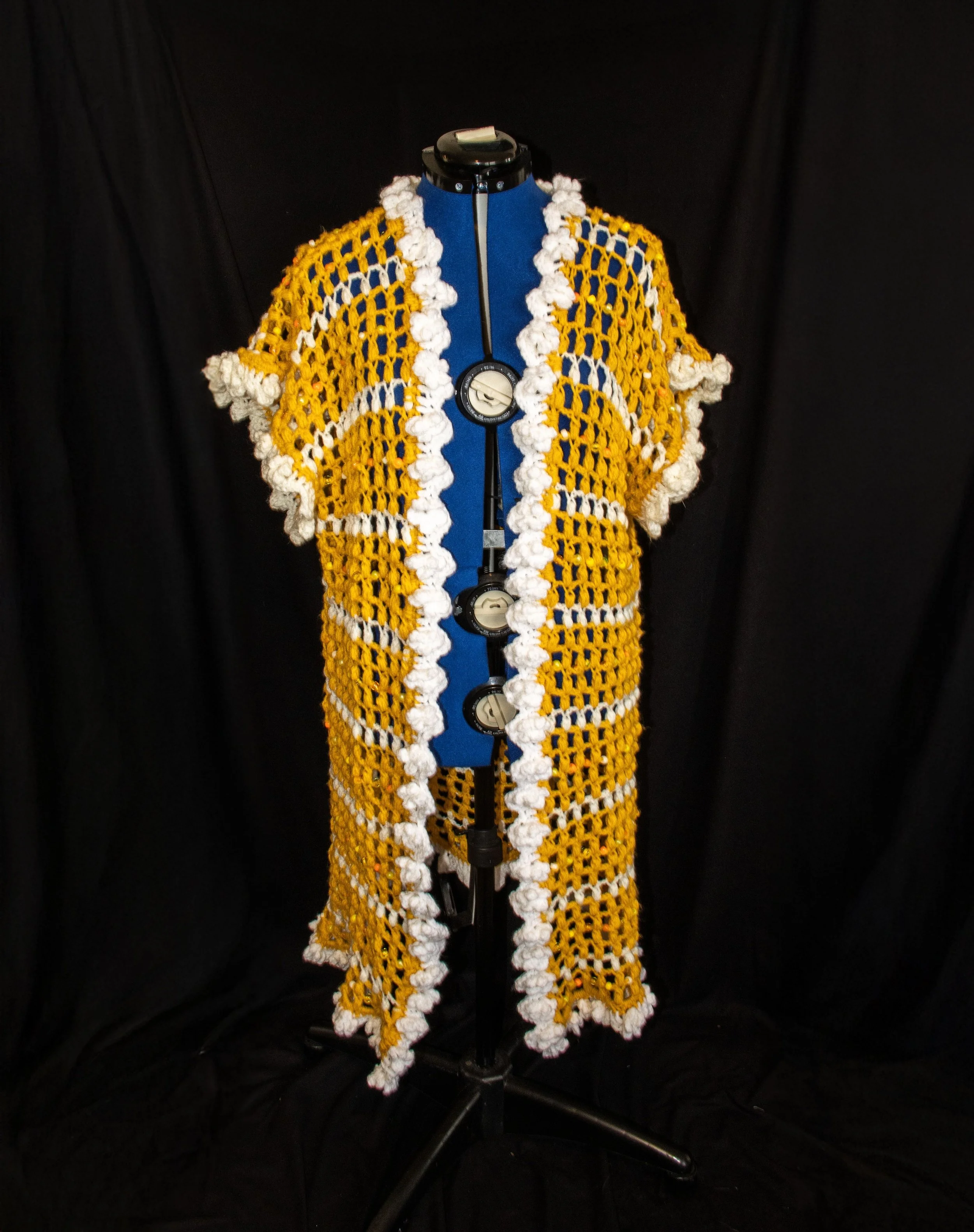 A colorful crochet garment displayed on a mannequin with a black background.