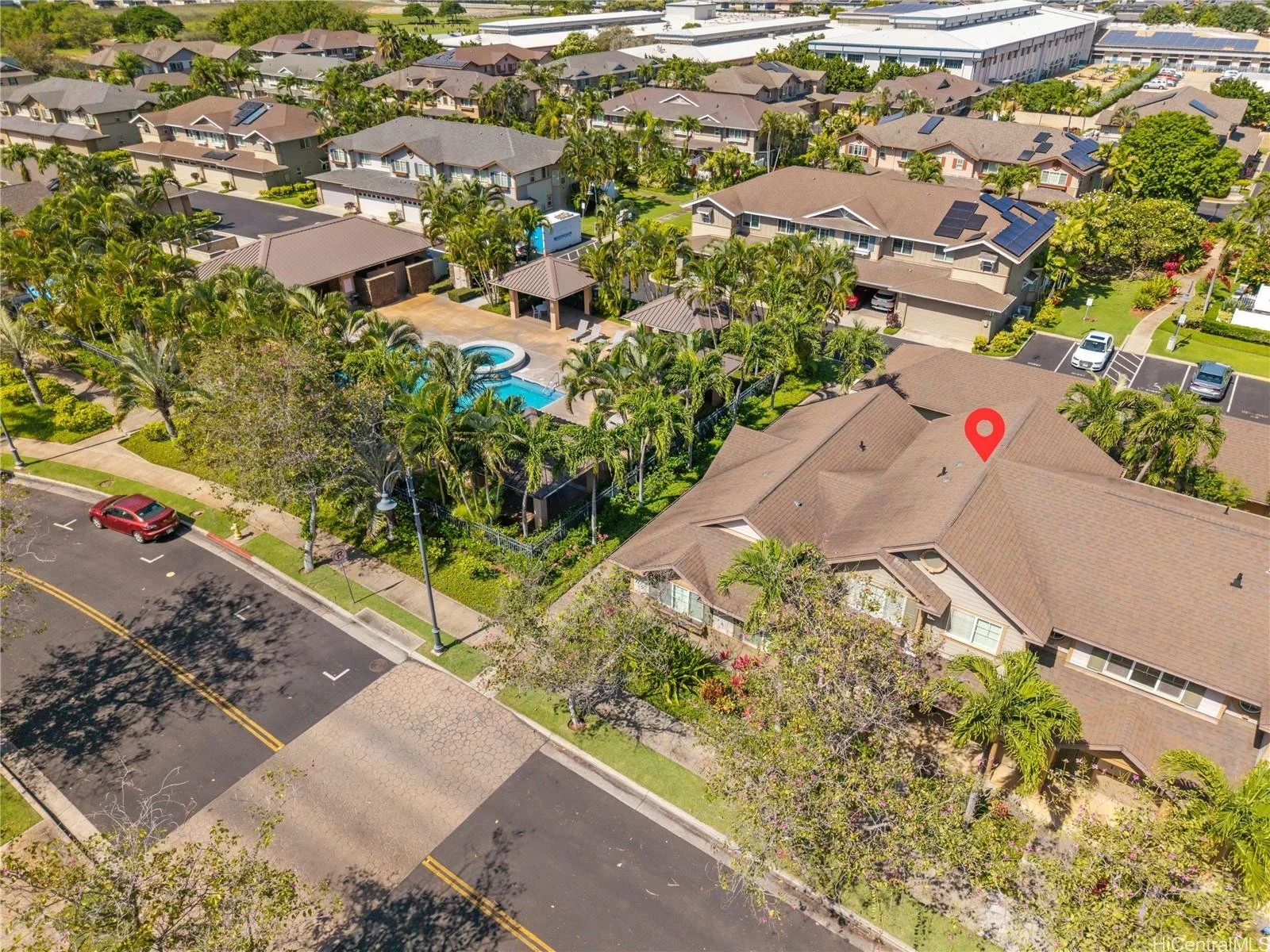 Aerial view of a suburban neighborhood with houses, palm trees, and a swimming pool in the backyard, with a street and parked cars in the foreground.