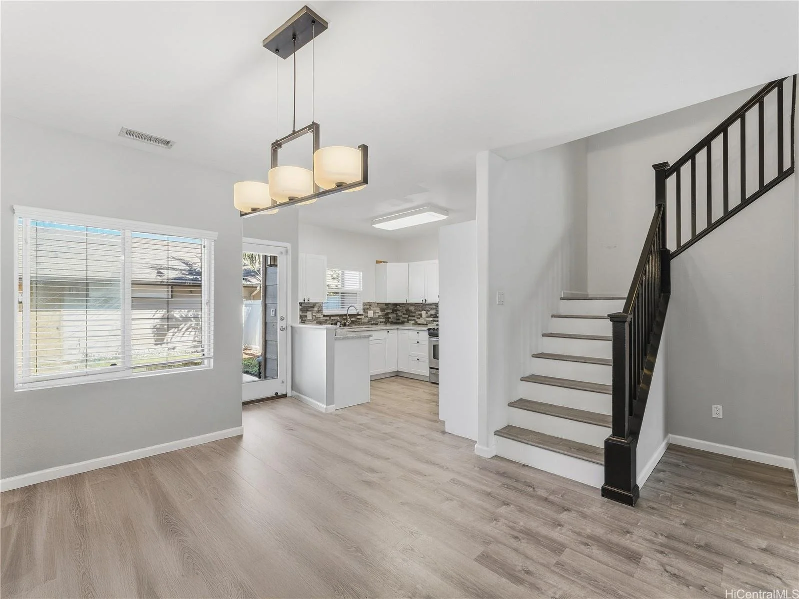 Interior view of a modern kitchen and dining area with a staircase, large window, and light-colored wood flooring.