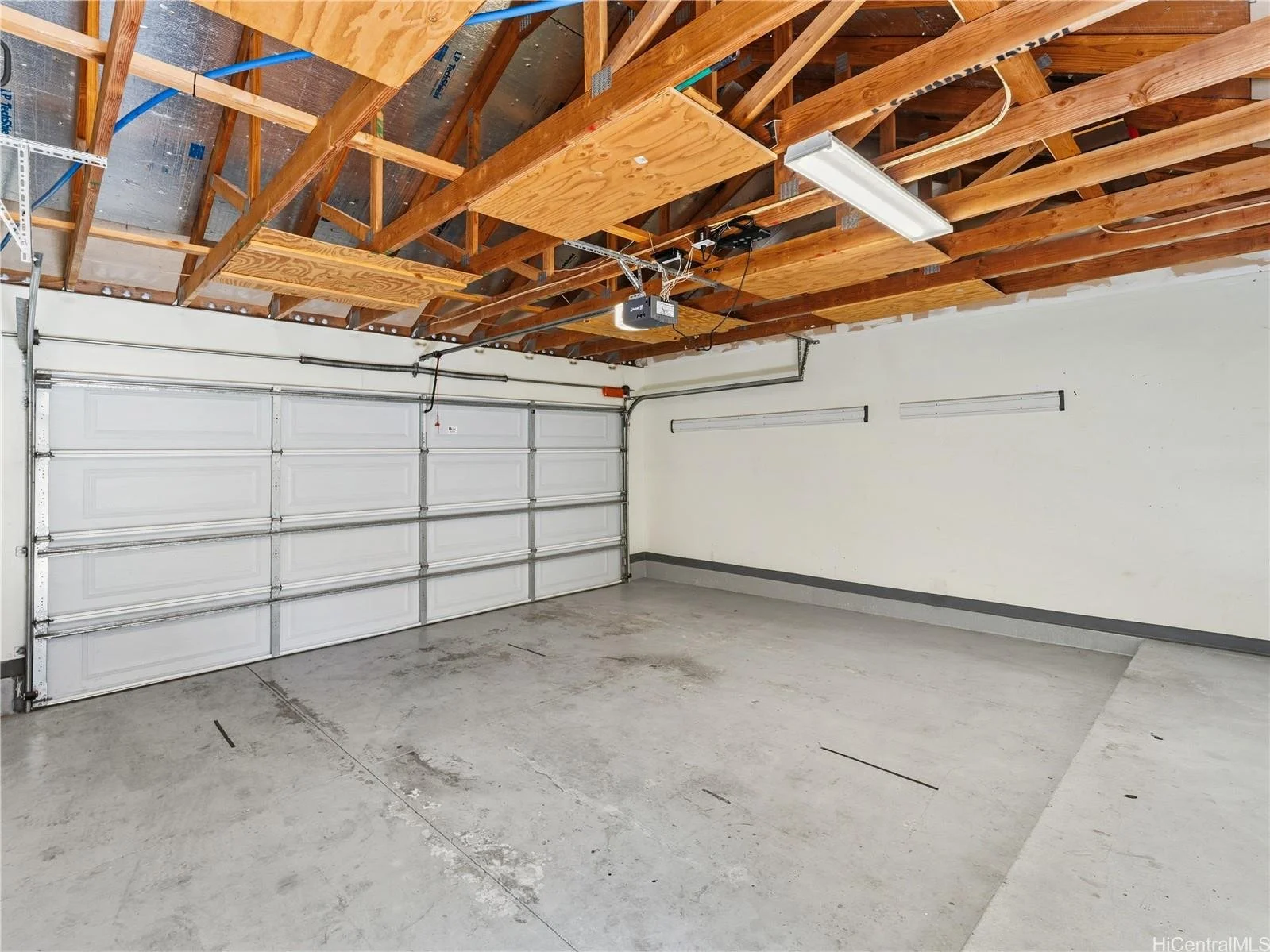 Empty garage with concrete floor, white walls, a white garage door, a fluorescent ceiling light, and exposed wooden ceiling rafters.