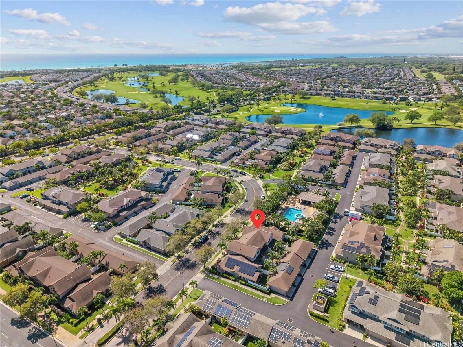 Aerial view of a suburban neighborhood with houses, streets, and greenery, near a golf course and water bodies, with the ocean in the background.