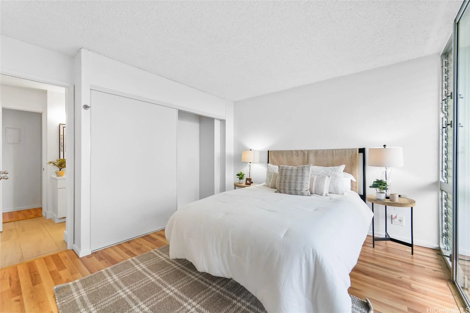 A bedroom with a bed, two bedside tables with lamps, a sliding glass door, and hardwood floors.