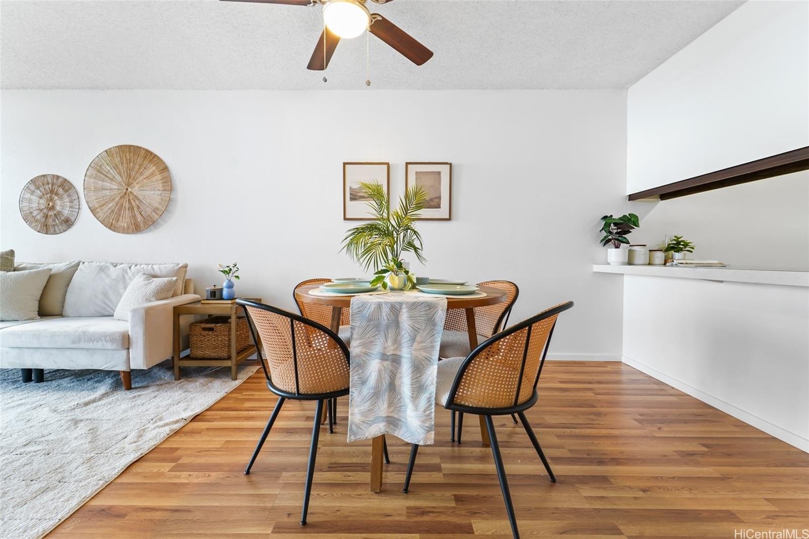 Open-concept living and dining area with a round wooden table, four chairs, a white sofa, wall art, and decorative elements in a modern, minimalist style.