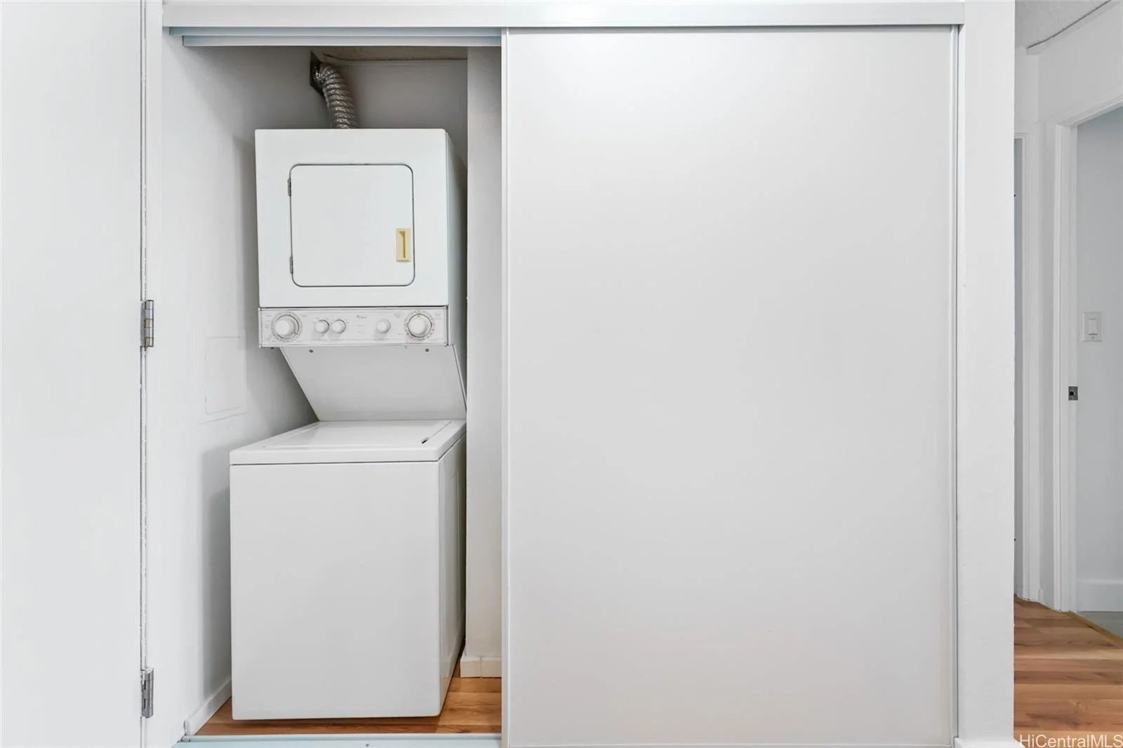 White stacked washer and dryer unit in a laundry closet with a sliding door