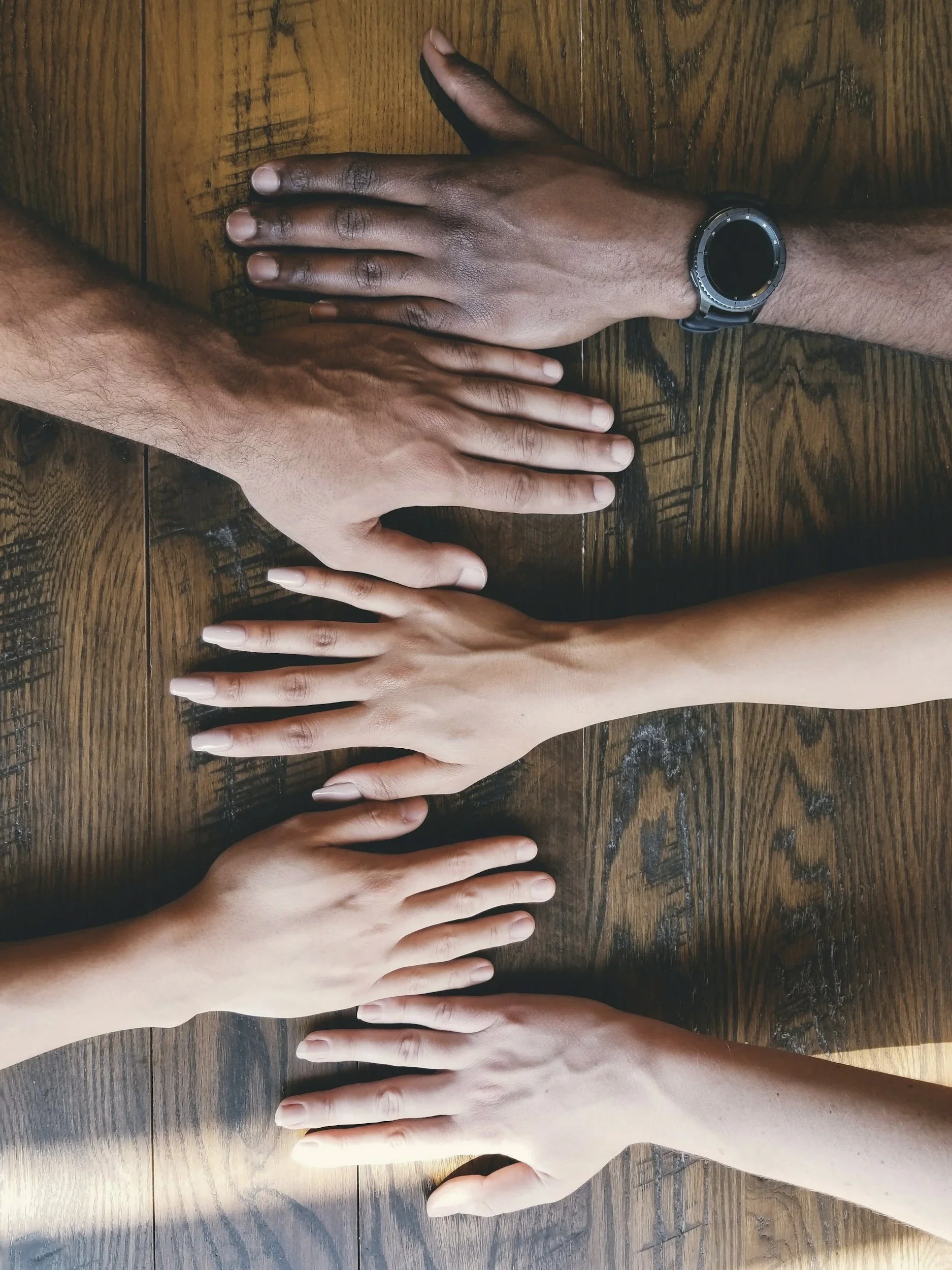 wooden table background with a diverse group of hands laid out flat side by side representing community and diversity