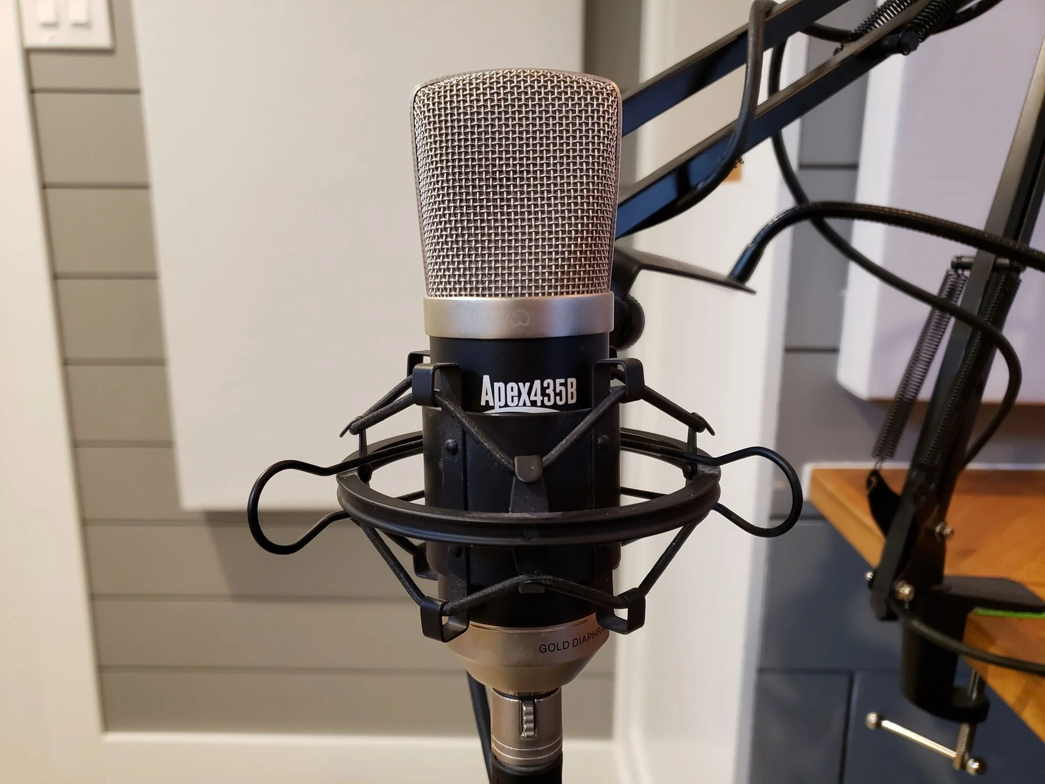 Close-up of a professional recording microphone mounted on a stand with a pop filter, positioned in a studio or audio recording setup.