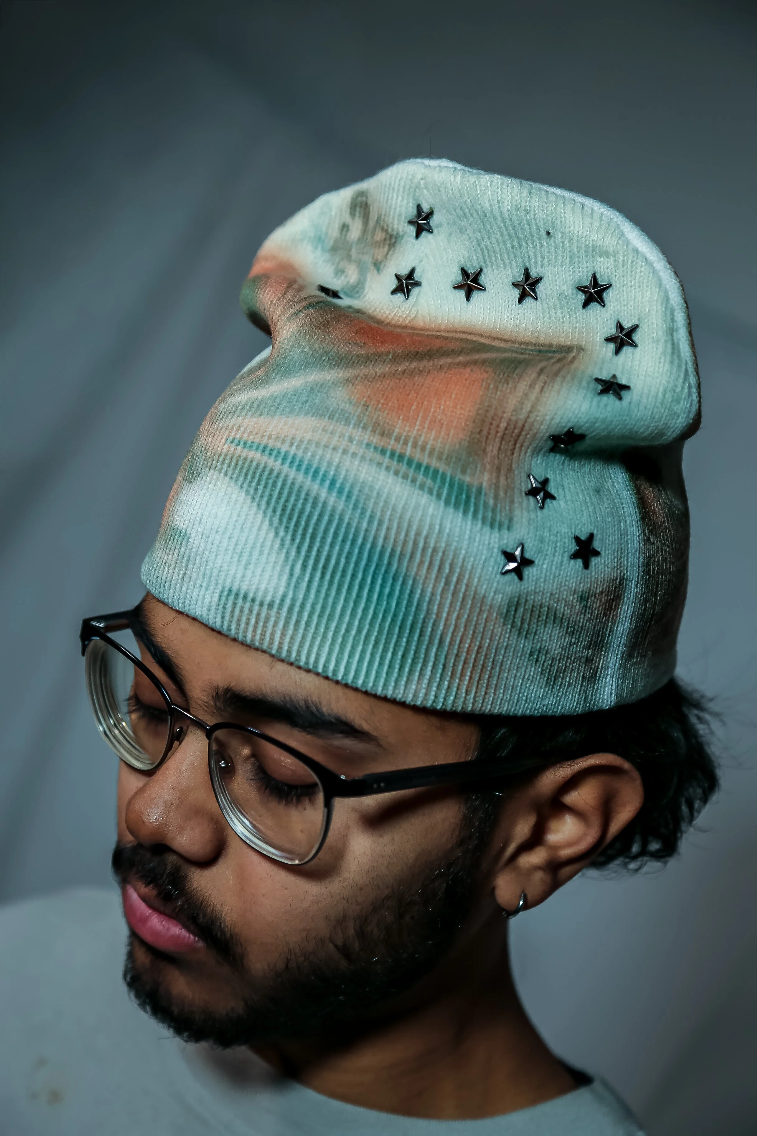 A person wearing glasses and a colorful tie-dye beanie with star-shaped embellishments.