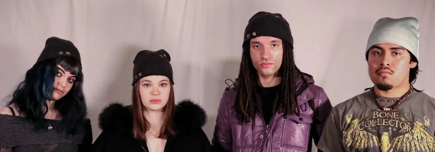 Four young adults standing side by side against a plain background, wearing casual streetwear including beanies, with various facial expressions.