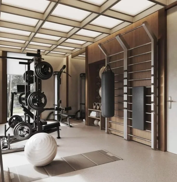 A modern home gym with various exercise equipment, including a weightlifting machine, a punching bag, a large exercise ball, and a wall-mounted ladder with fitness accessories.