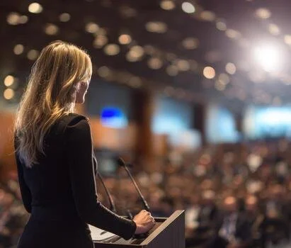 Female speaker addressing large (out of focus) audience