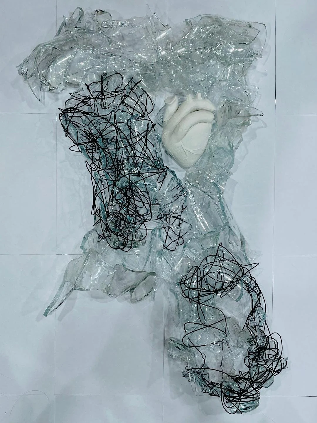 An art sculpture of a human heart surrounded by broken glass and black metal wire.
