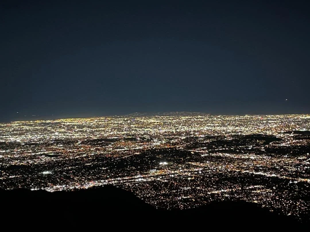 Nighttime aerial view of a city illuminated with bright lights, seen from a high vantage point, with a dark sky overhead.